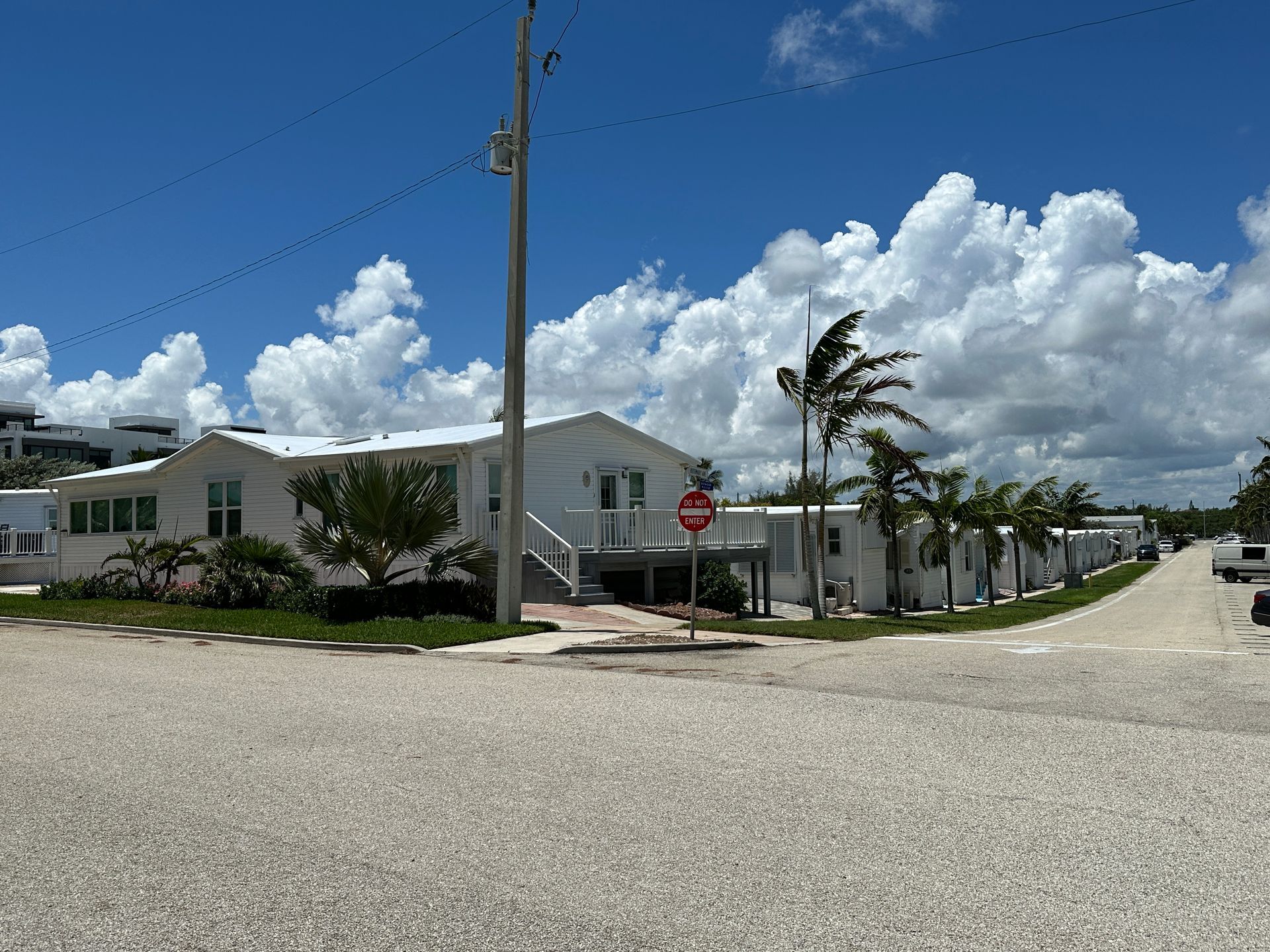 White buildings on a gravel road under a blue sky with puffy white clouds.