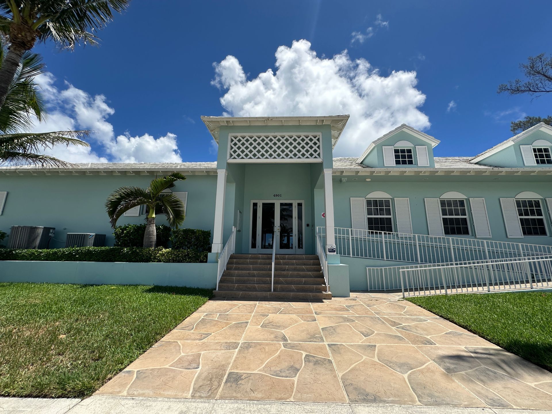 Blue building with white trim and shutters, stone path, steps, and blue sky.