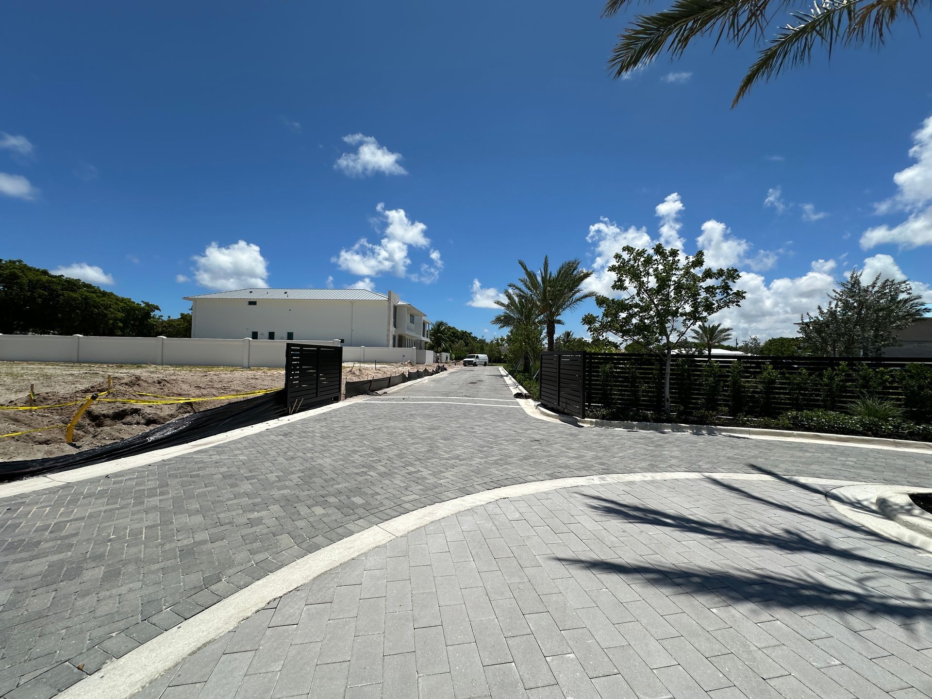 Paved road with a white trimmed building in the distance, under a blue sky with scattered clouds.