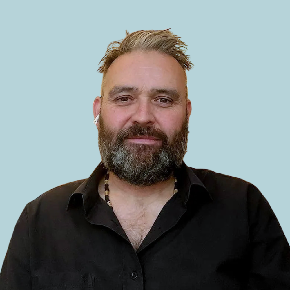 Man with salt-and-pepper beard wearing black shirt; light blue background.