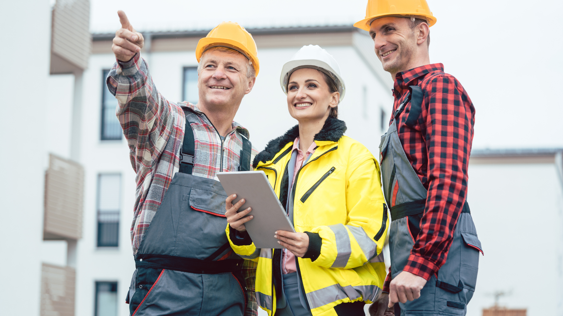 Construction workers in hard hats reviewing a tablet on a building site.
