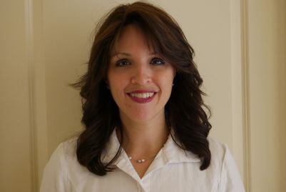 A woman in a white shirt and necklace is smiling for the camera.