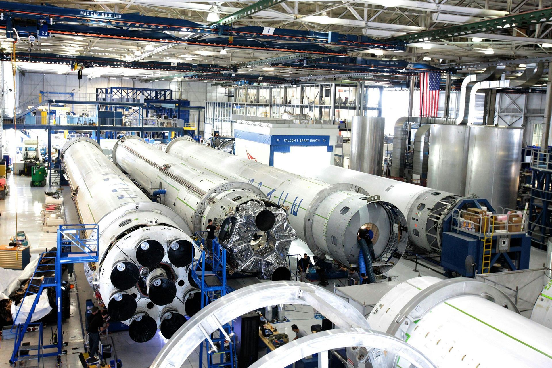 Inside a large manufacturing building, multiple rocket stages are under assembly.