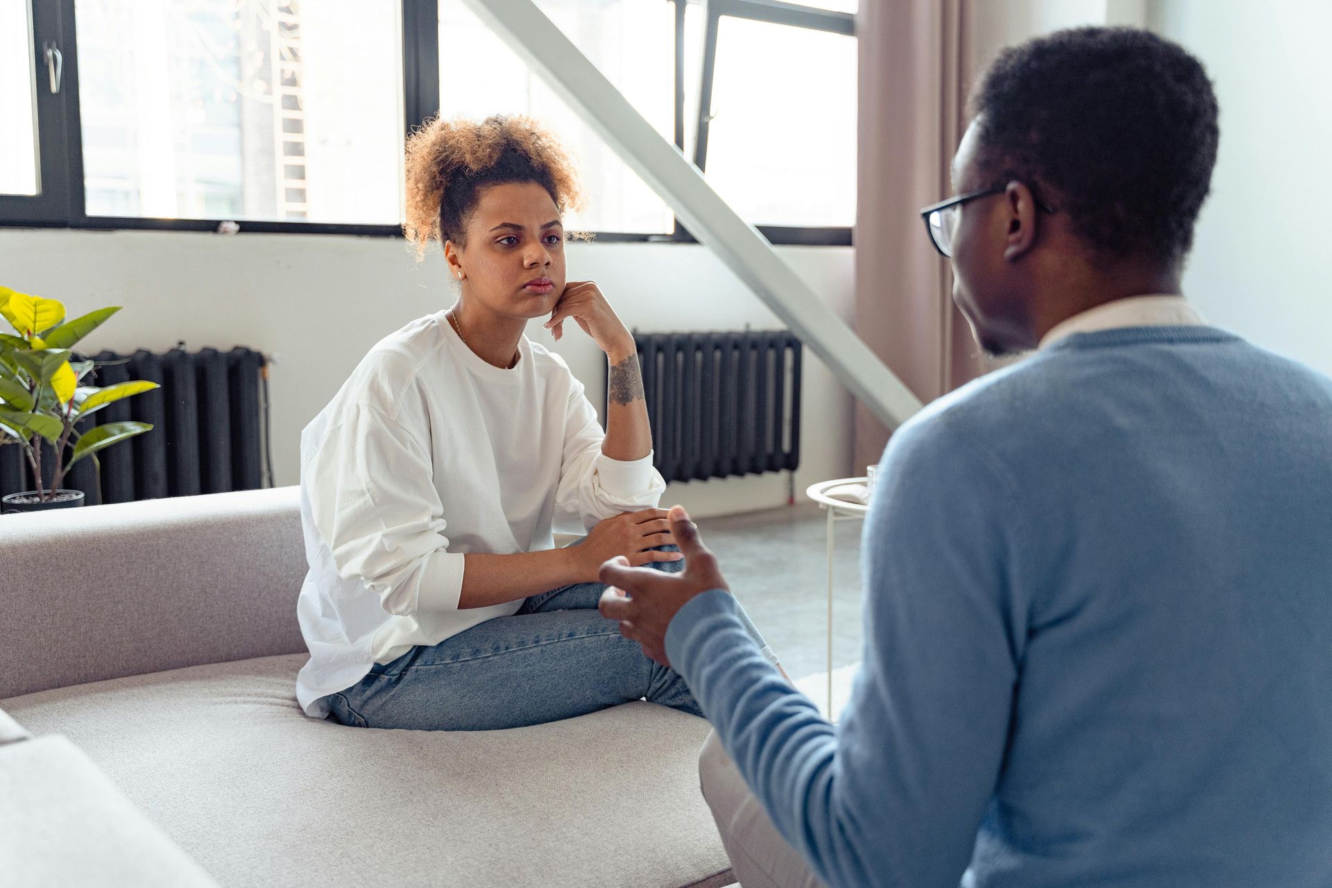 Woman on couch talking to a person in a light blue sweater; indoor setting.