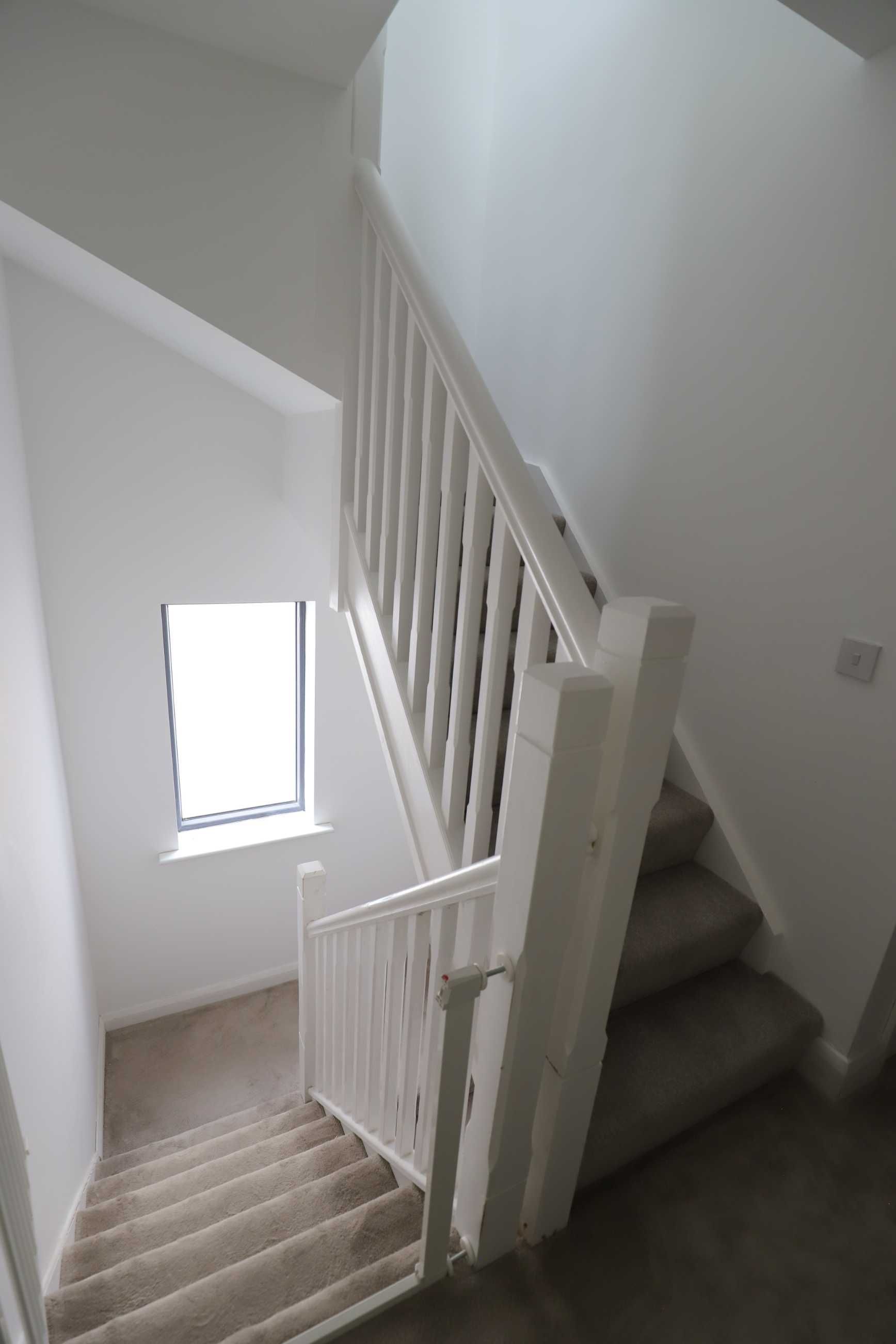 A staircase in a house with a white railing and a window.