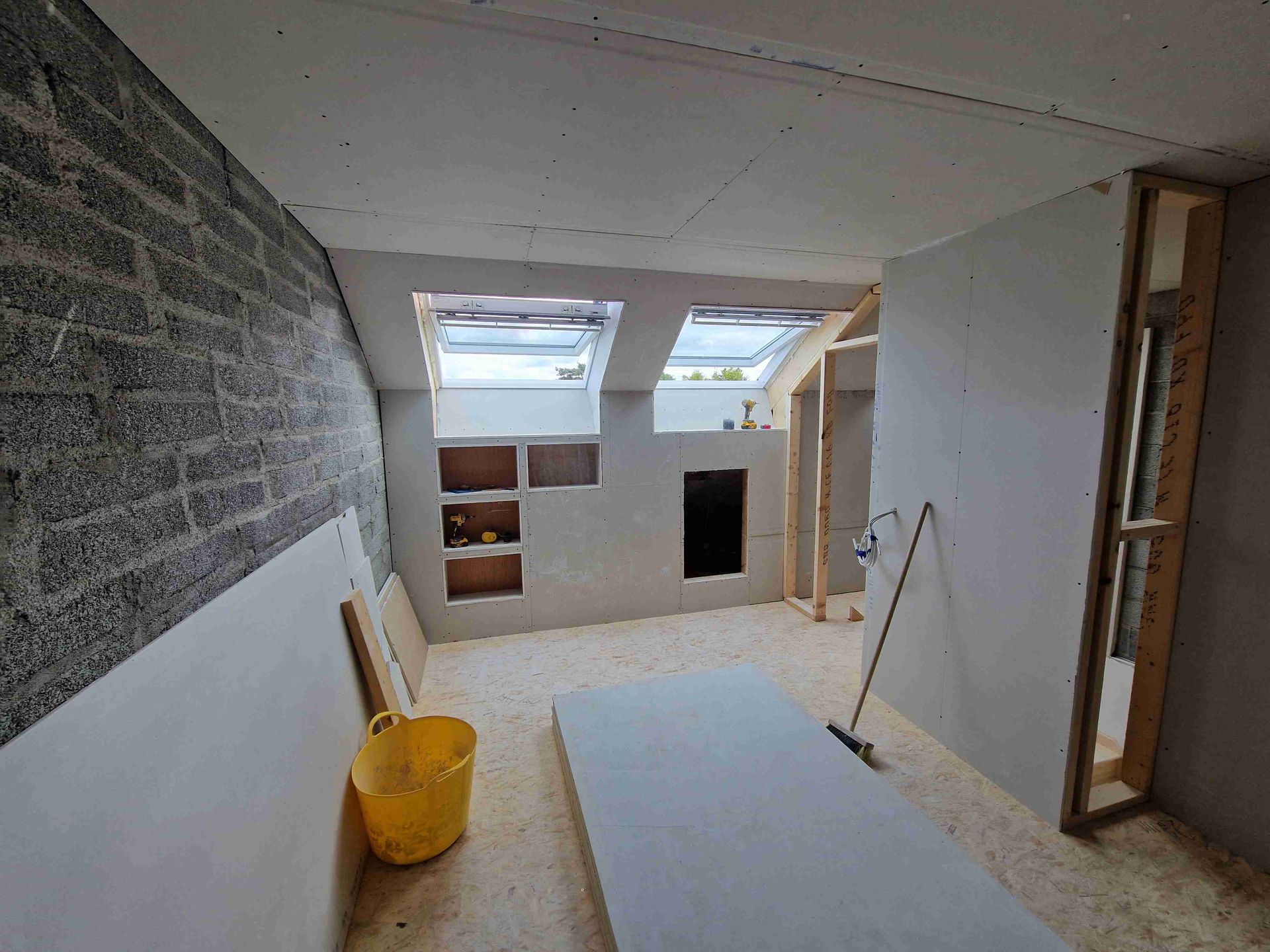 A room under construction with a yellow bucket and a broom.