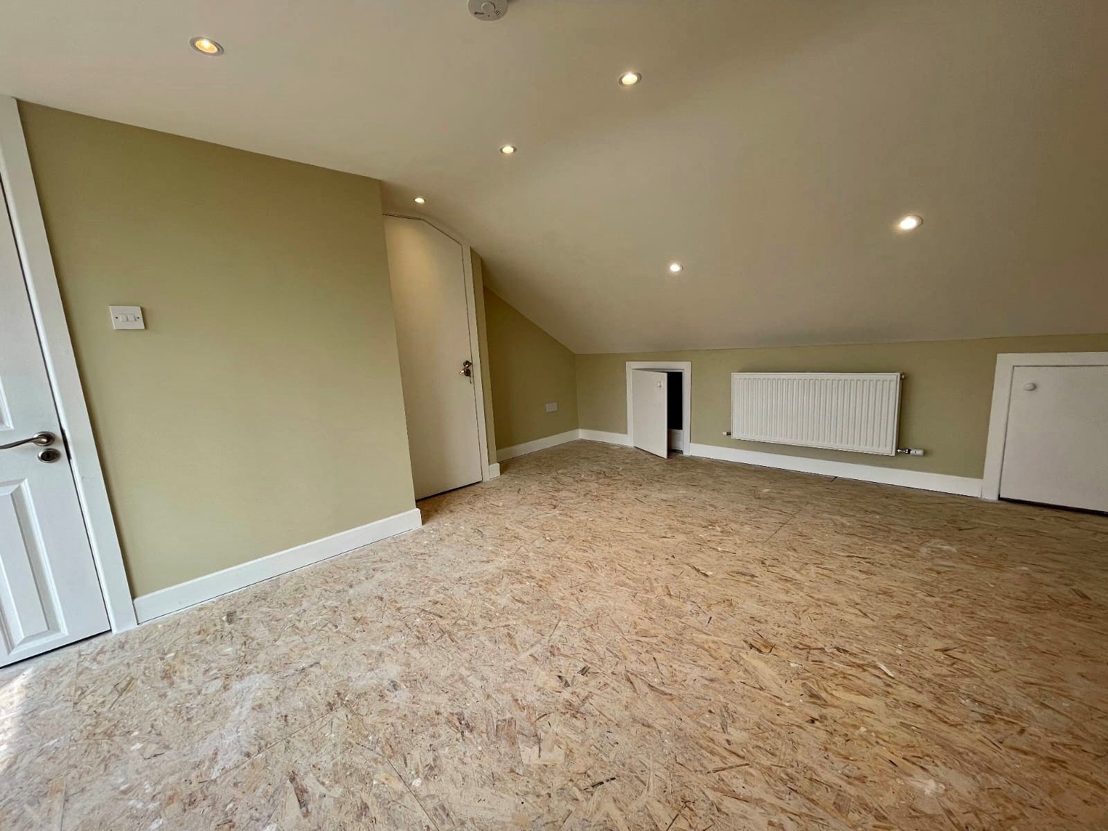 An empty room with a vaulted ceiling and a carpeted floor.