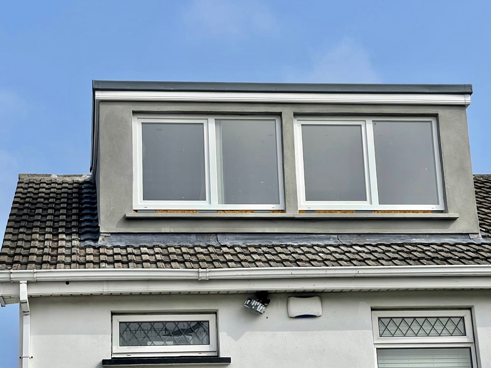 The roof of a house with three windows and a blue sky in the background