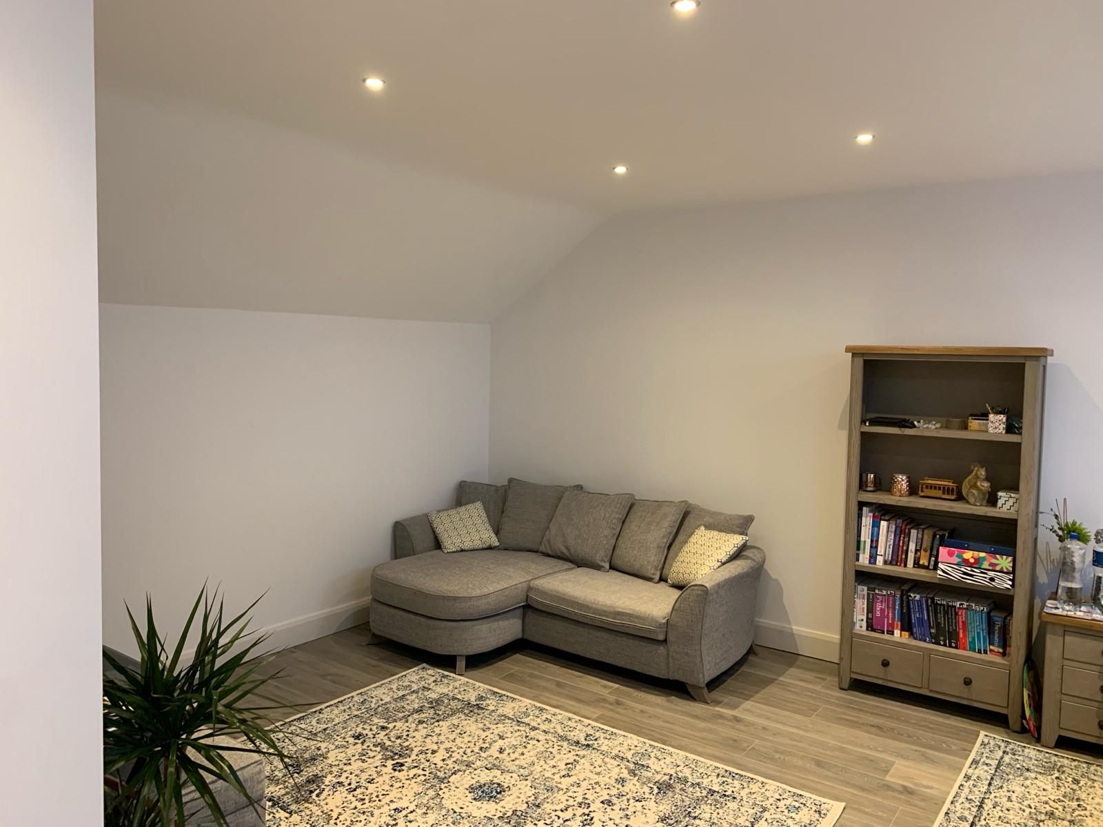A living room with a sectional couch and a bookshelf.