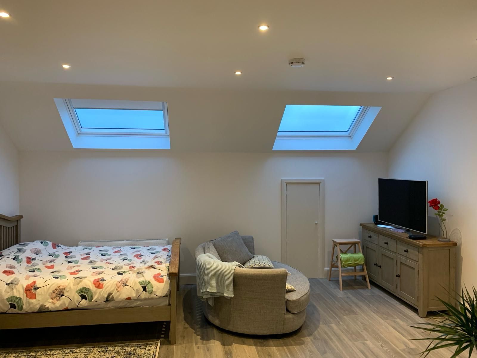 A bedroom with a bed , couch , television and skylights.