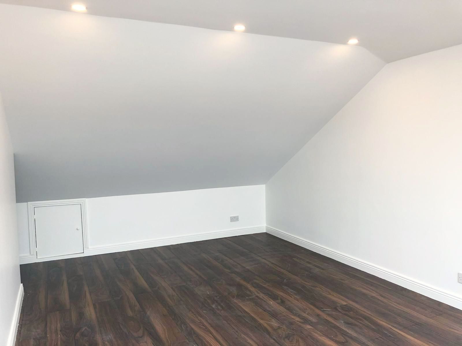 An empty room with a slanted ceiling and hardwood floors.