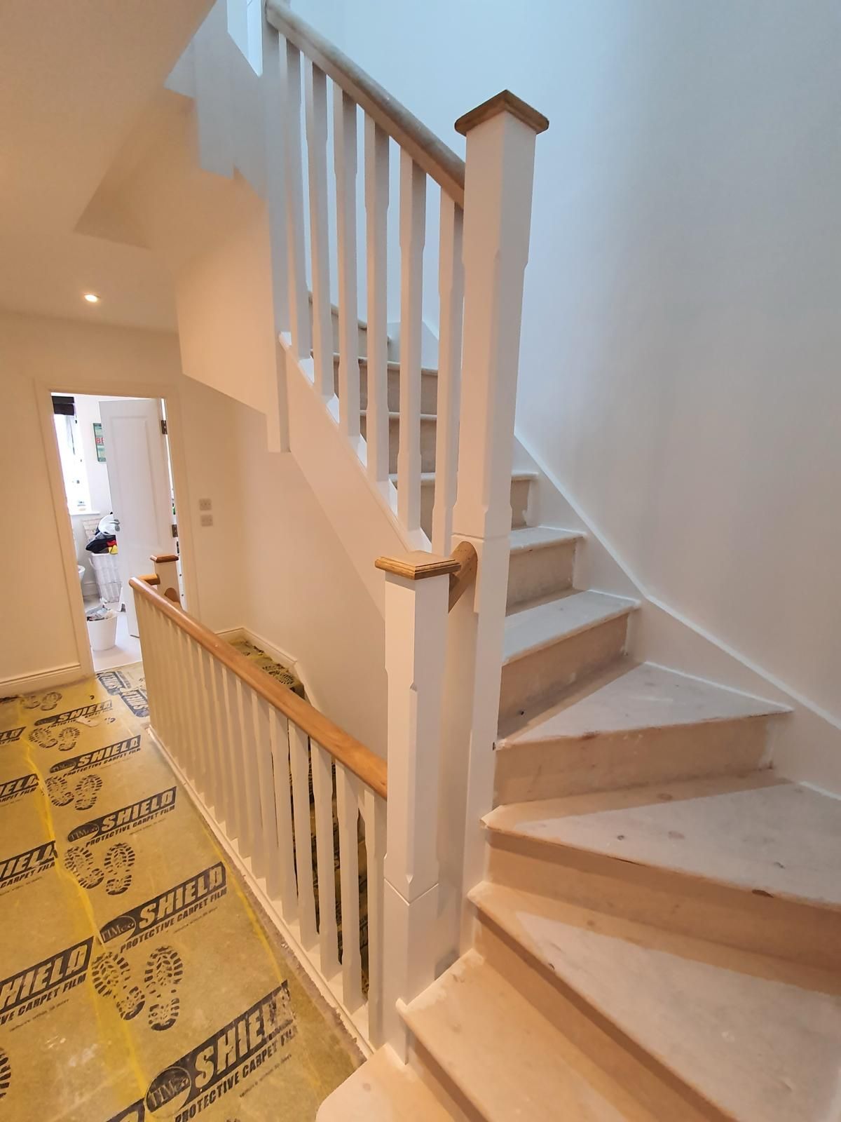 A staircase with a white railing and a yellow mat that says snickers on it.
