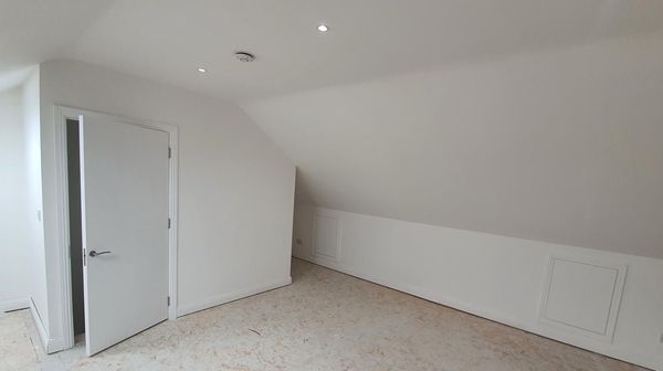 An empty room with a slanted ceiling and a door.