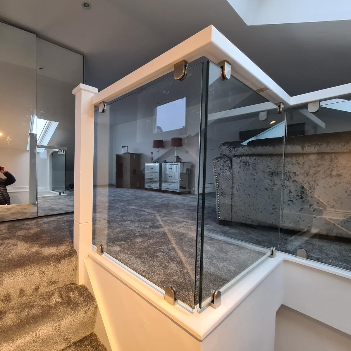 A person is taking a picture of a staircase with a glass railing.