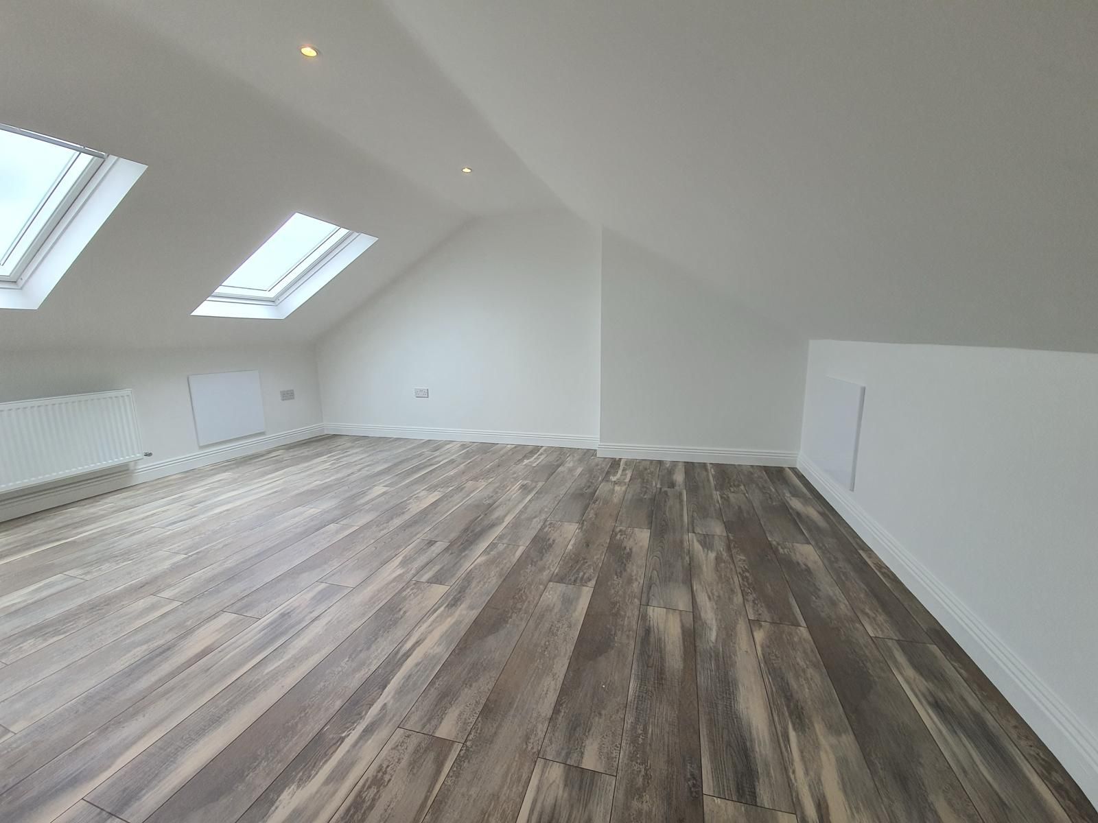 An empty room with hardwood floors and a skylight in the ceiling.