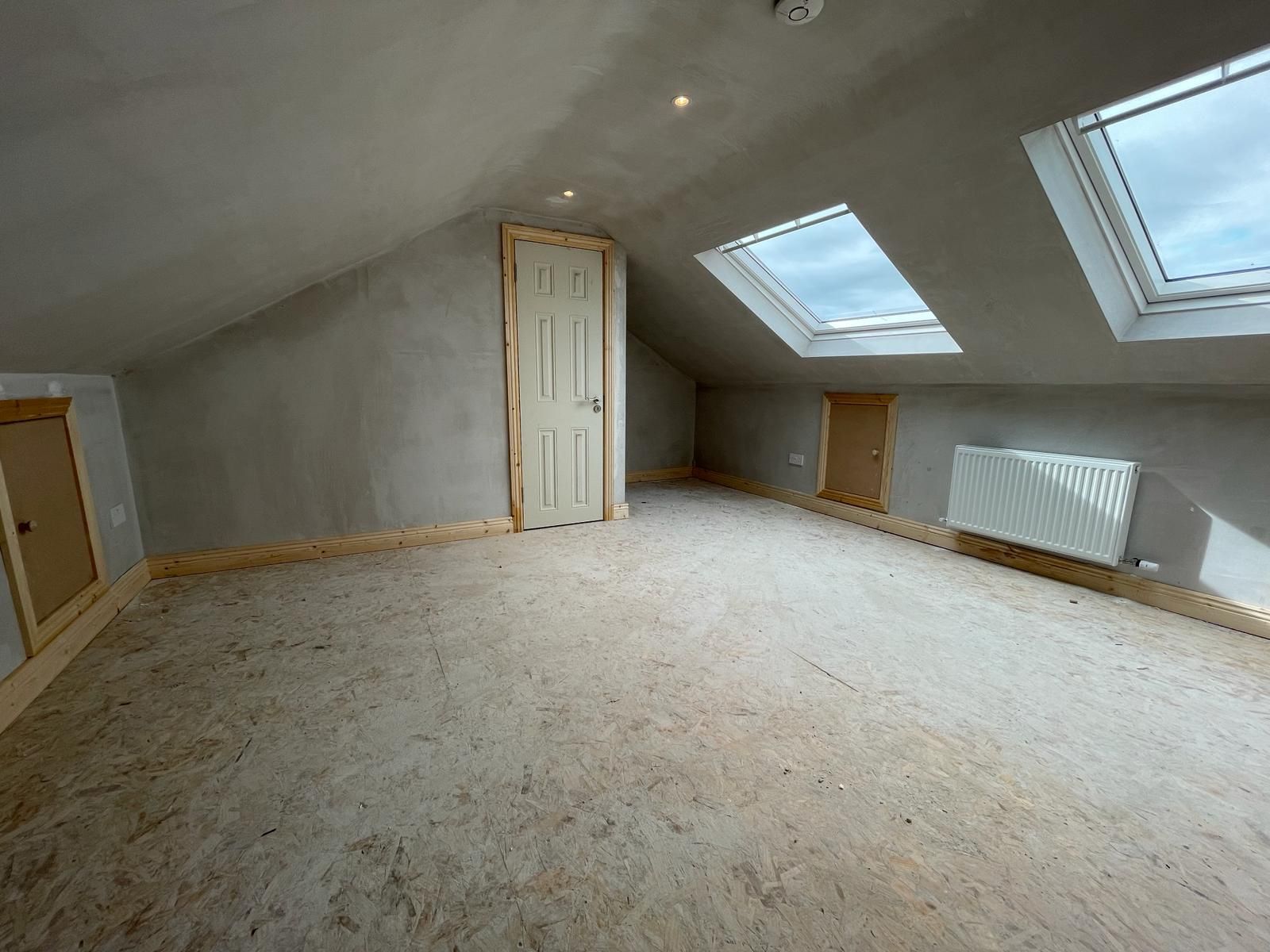 An empty attic with two skylights and a door.