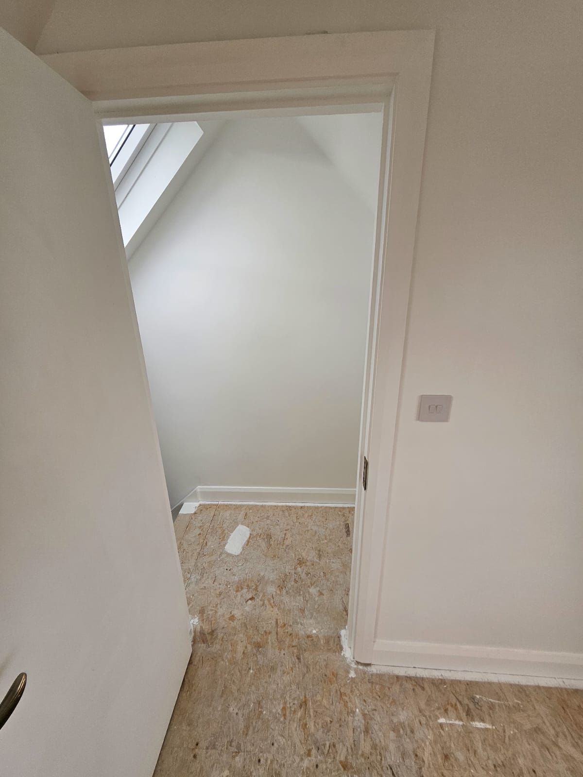 A room with a door open and a window in the ceiling.