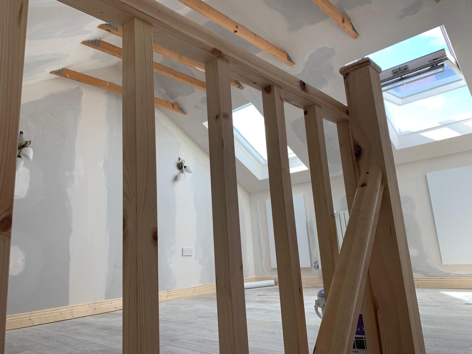 A wooden railing in an empty room with a skylight in the ceiling.