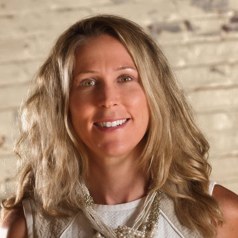 A woman wearing a white shirt and a necklace smiles for the camera