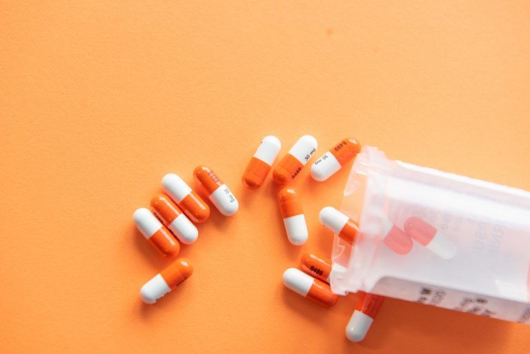 Orange and white pills are pouring out of a bottle on an orange background.