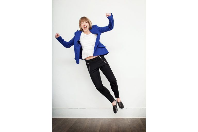 A woman in a blue jacket and black pants is jumping in the air.