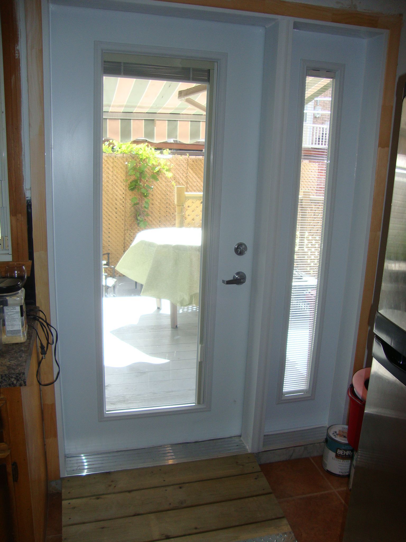 Double porte blanche à panneaux de verre donnant sur un patio avec une table et des plantes.
