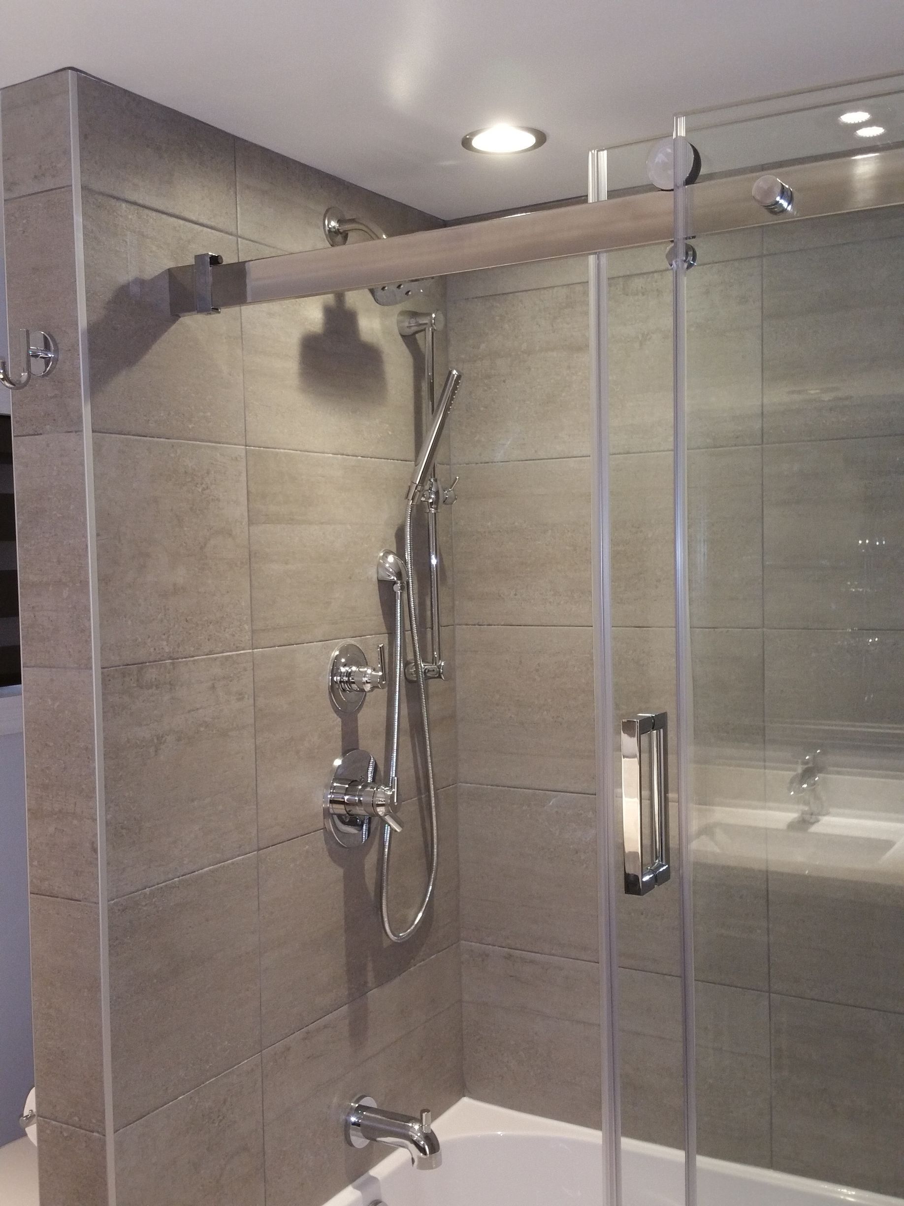 Douche avec porte en verre, murs carrelés et robinetterie argentée.