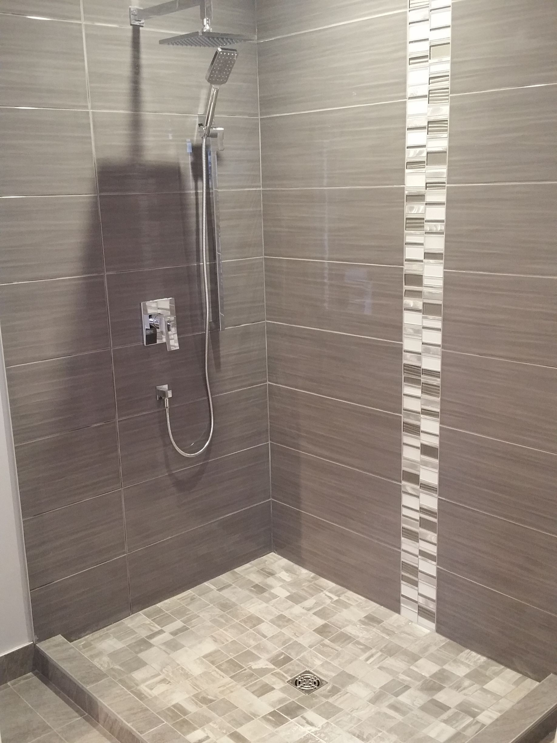 Cabine de douche avec carrelage marron et beige, pommeau de douche et frise décorative verticale.