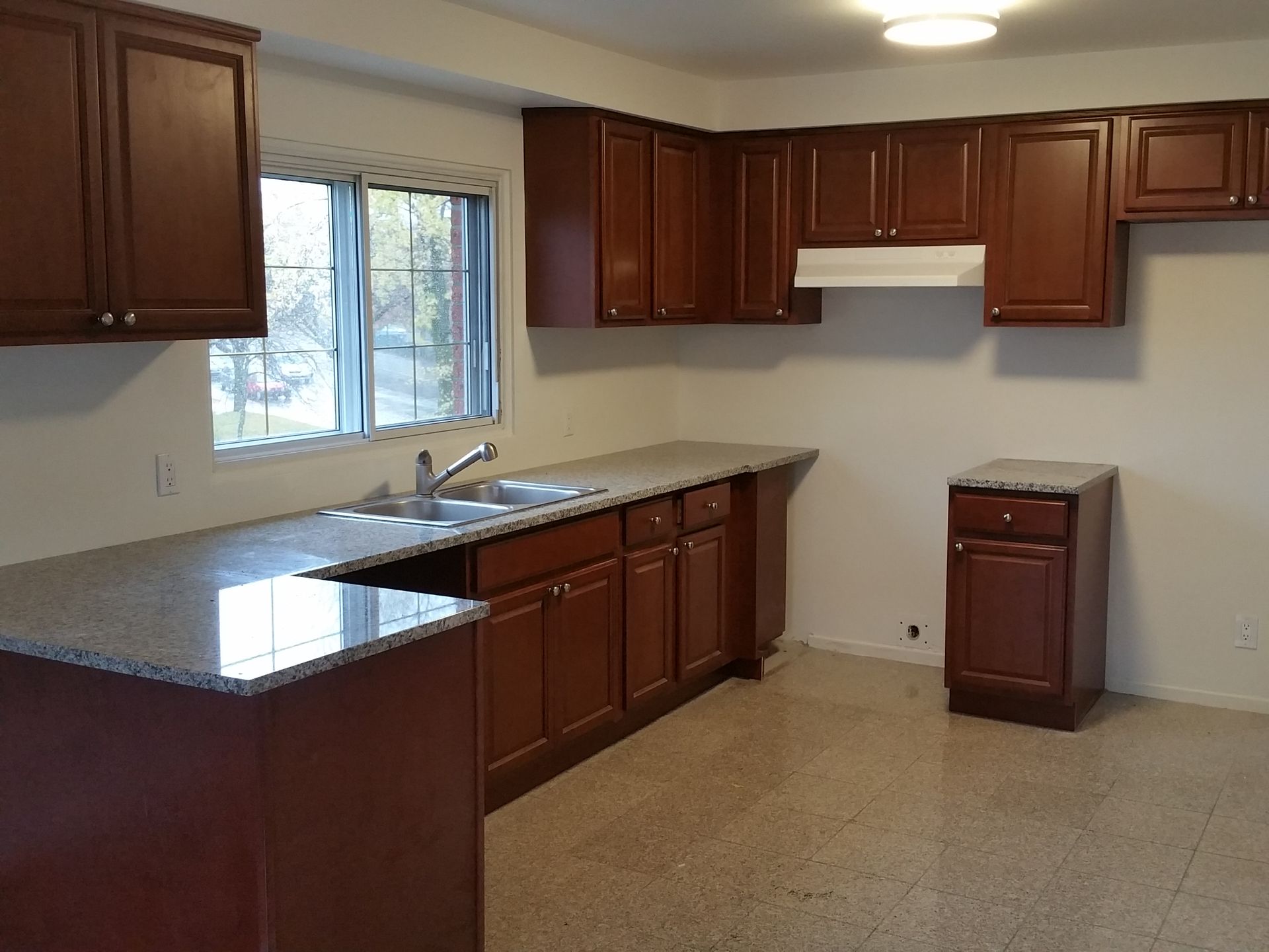 Cuisine avec placards marron, comptoirs gris et une fenêtre.