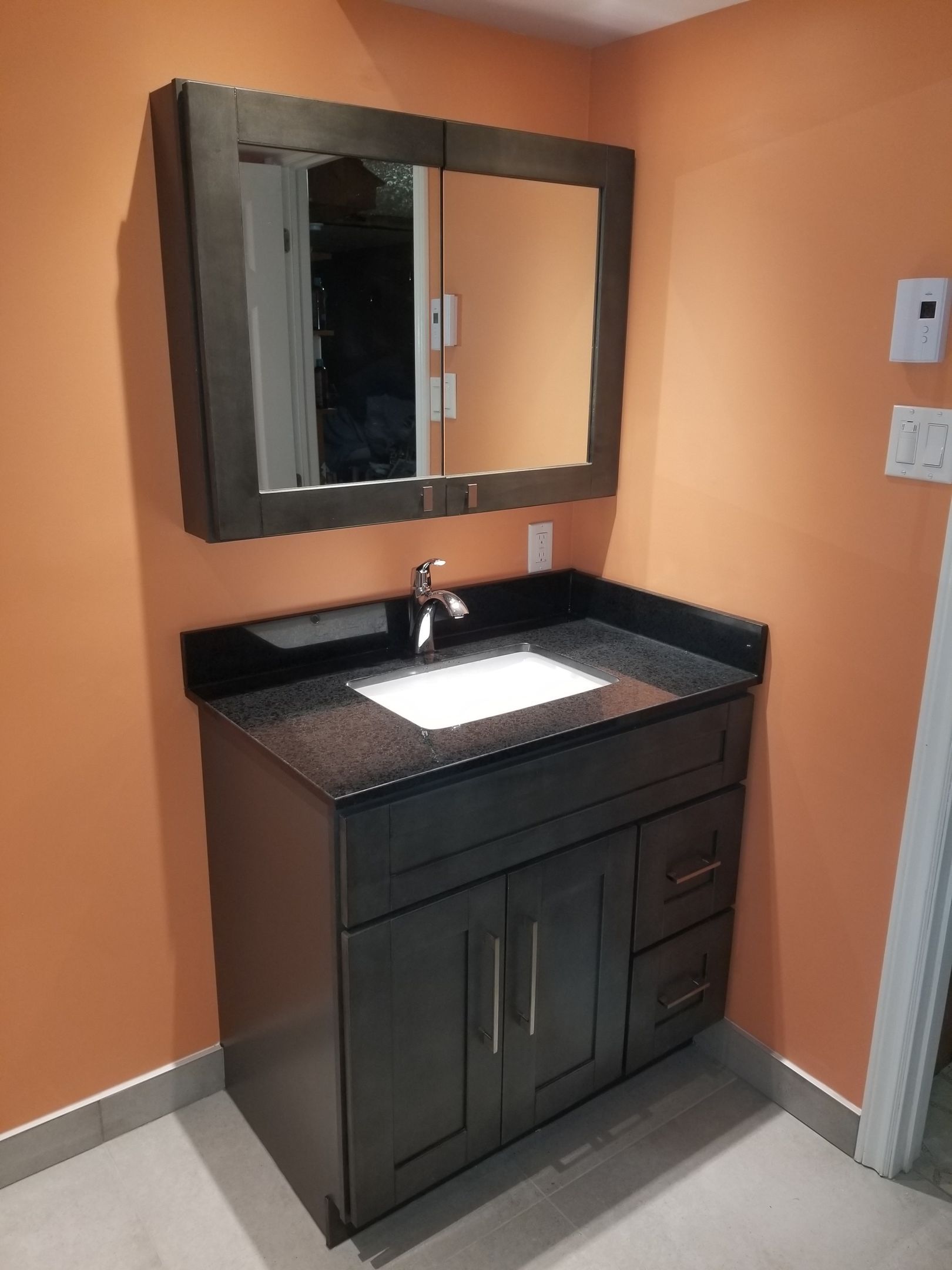 Salle de bains avec meuble-lavabo en bois foncé, comptoir noir, lavabo blanc, miroir et murs orange.