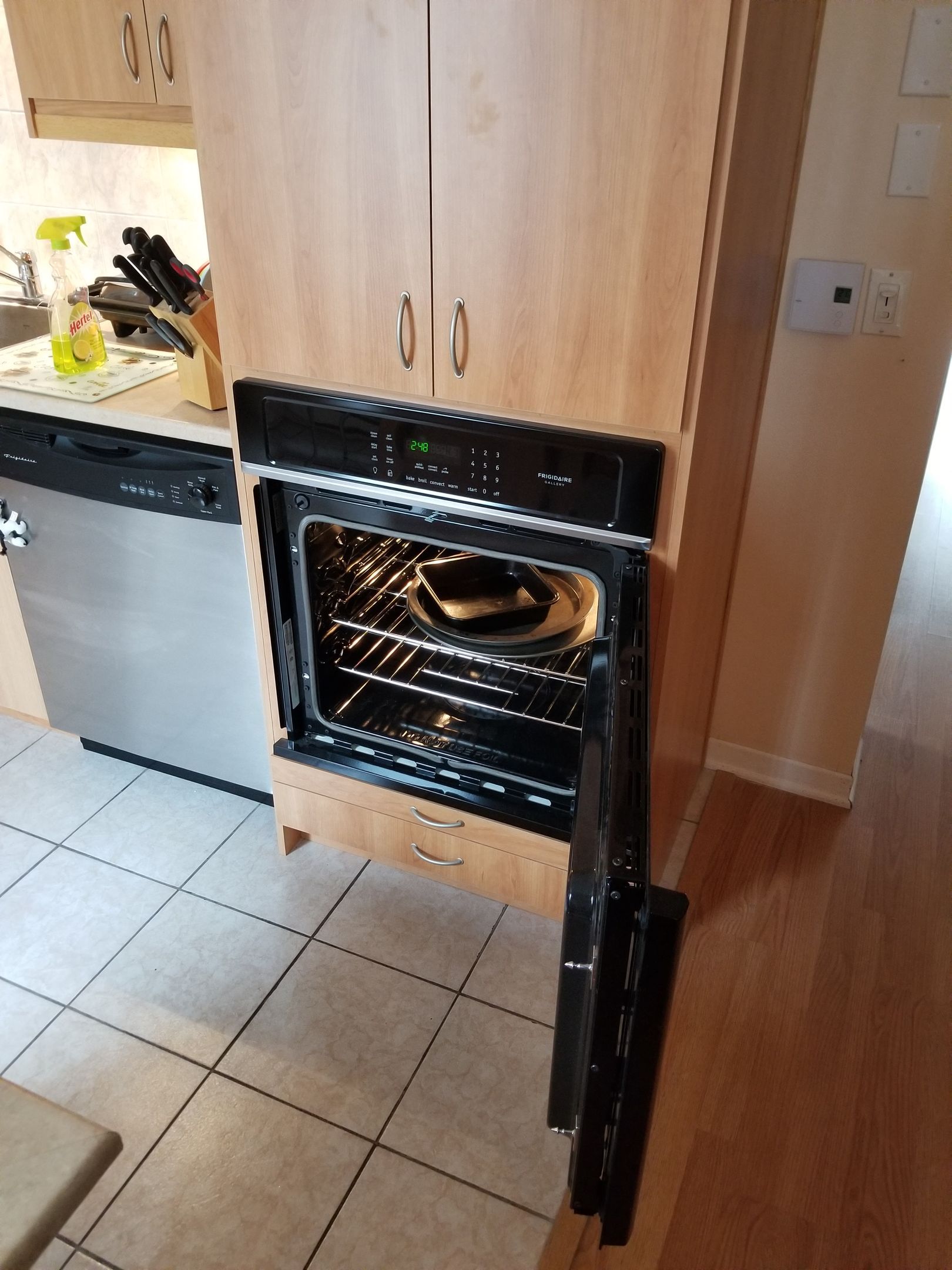 Four ouvert dans un meuble en bois clair, porte entrouverte. Intérieur du four noir visible, avec un petit objet sur la grille.