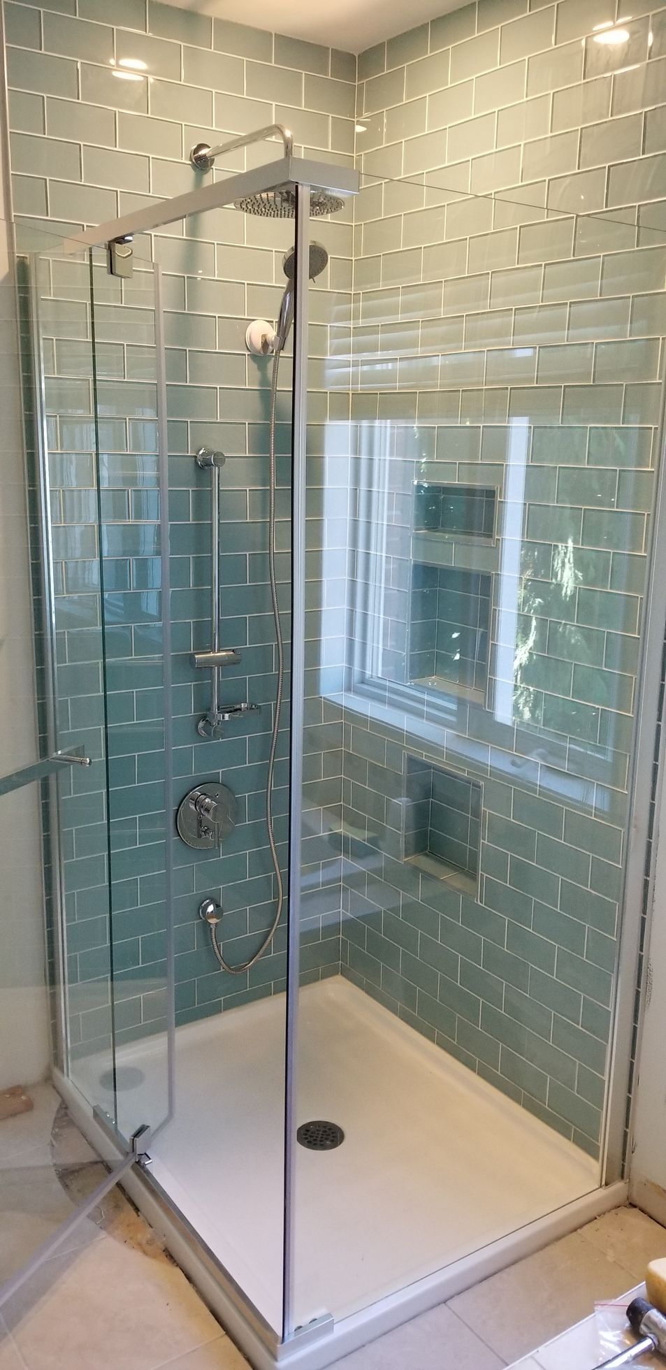 Une douche à l'italienne avec des murs carrelés de faïence métro bleu clair. Une grande porte vitrée et une fenêtre sont visibles.