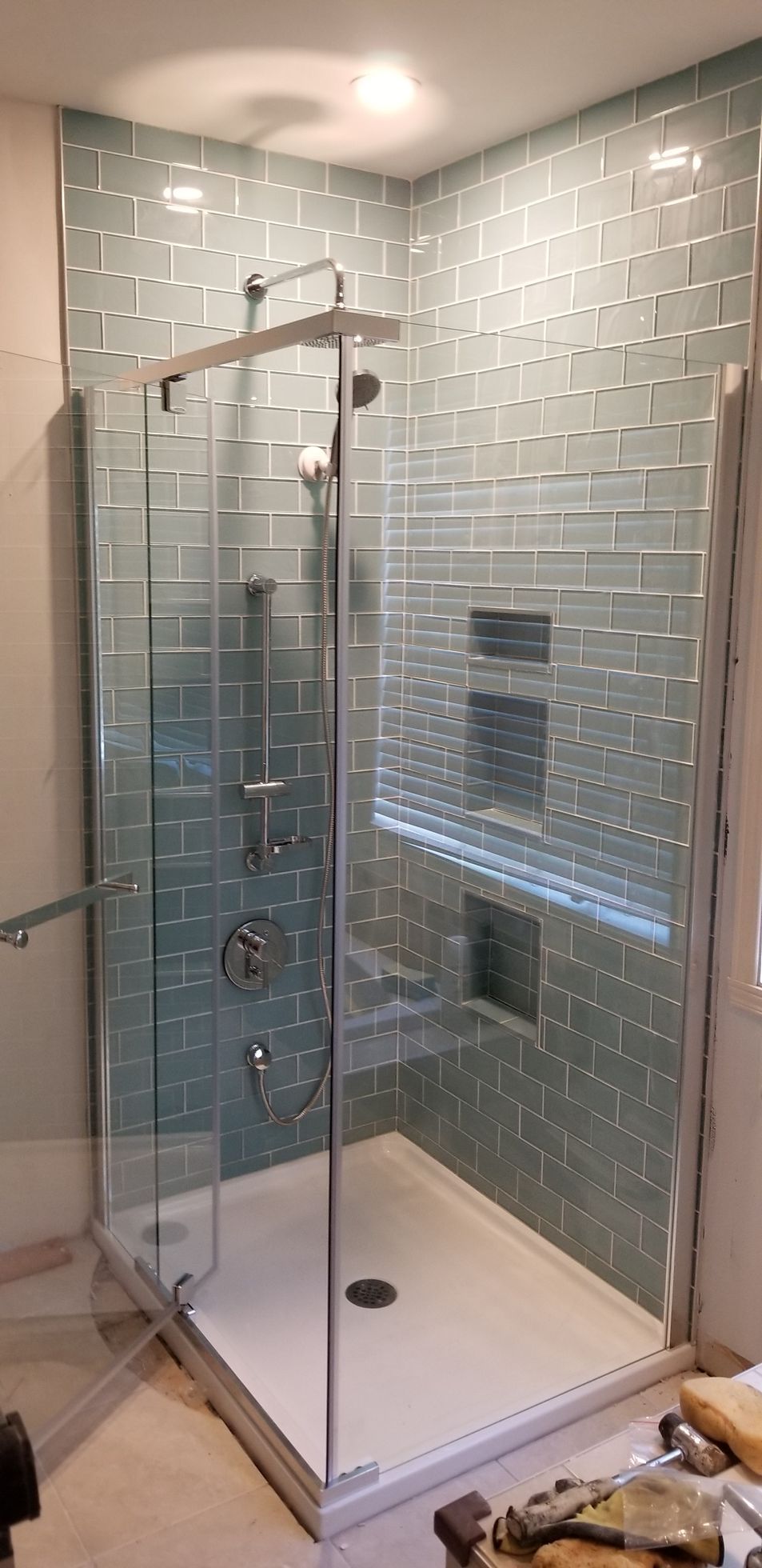Une douche récemment rénovée avec des portes en verre et des murs carrelés bleu turquoise.