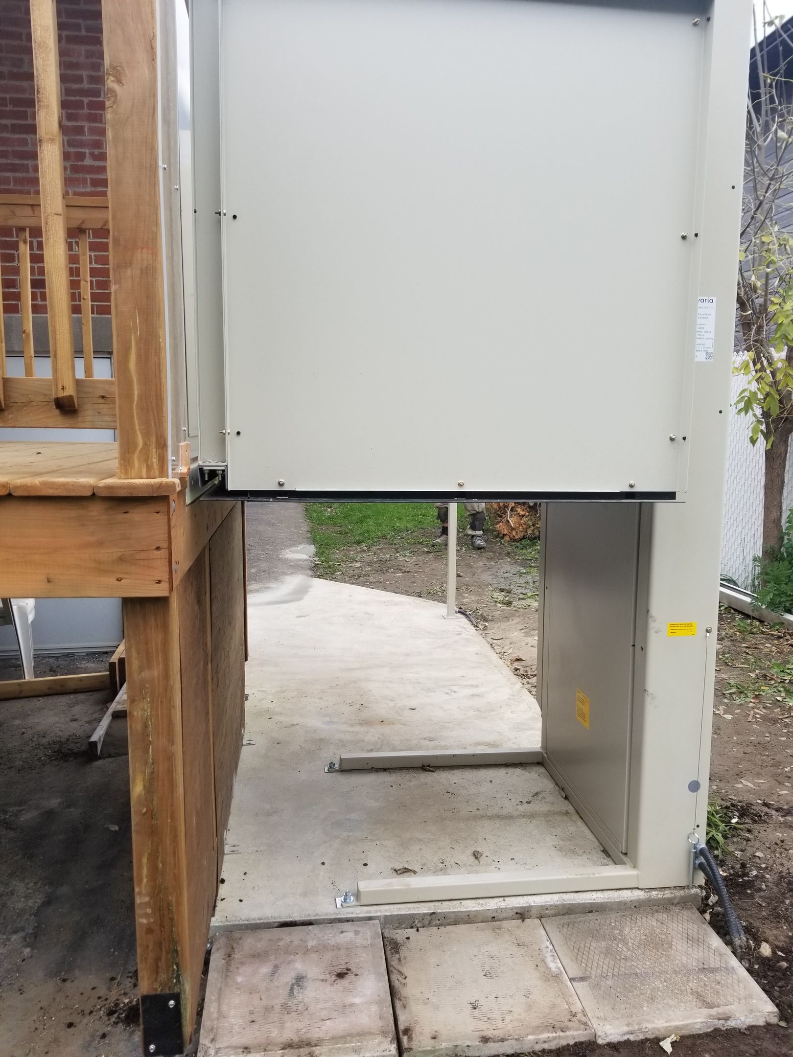 Ascenseur pour fauteuil roulant permettant l'accès d'une terrasse en bois à une allée en béton. Ascenseur beige à plateforme ouverte.