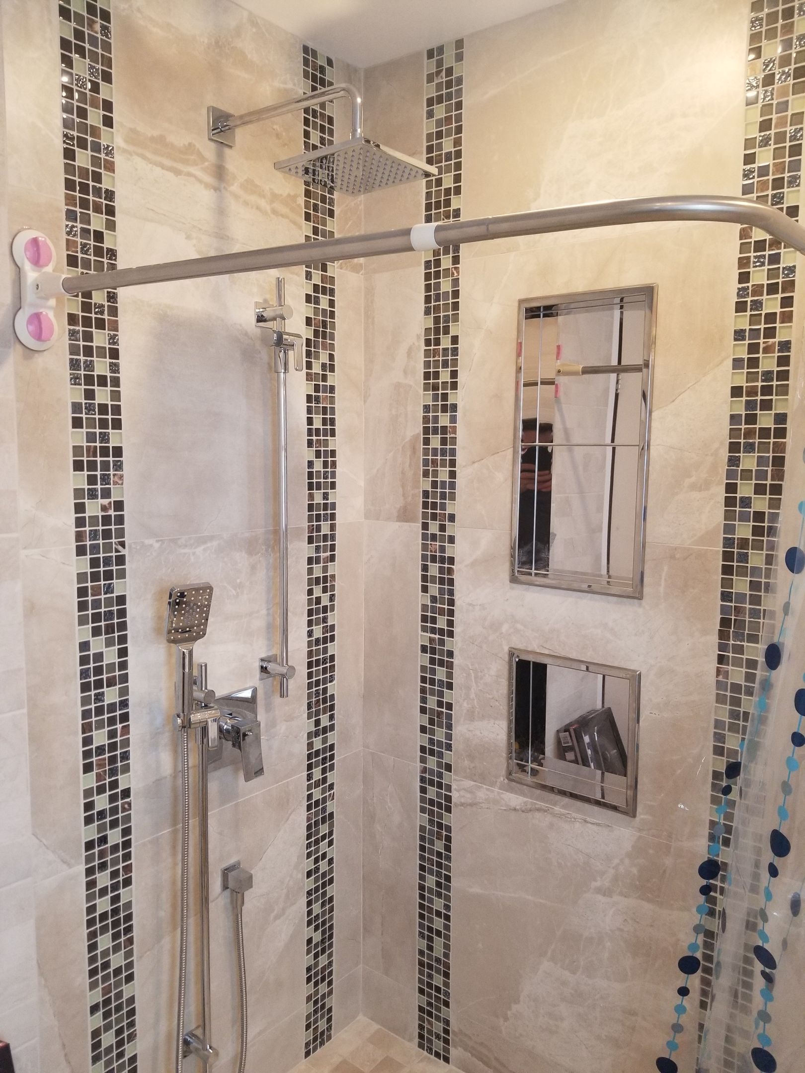 Douche avec robinetterie en acier inoxydable, accents de mosaïque et barre de douche incurvée.