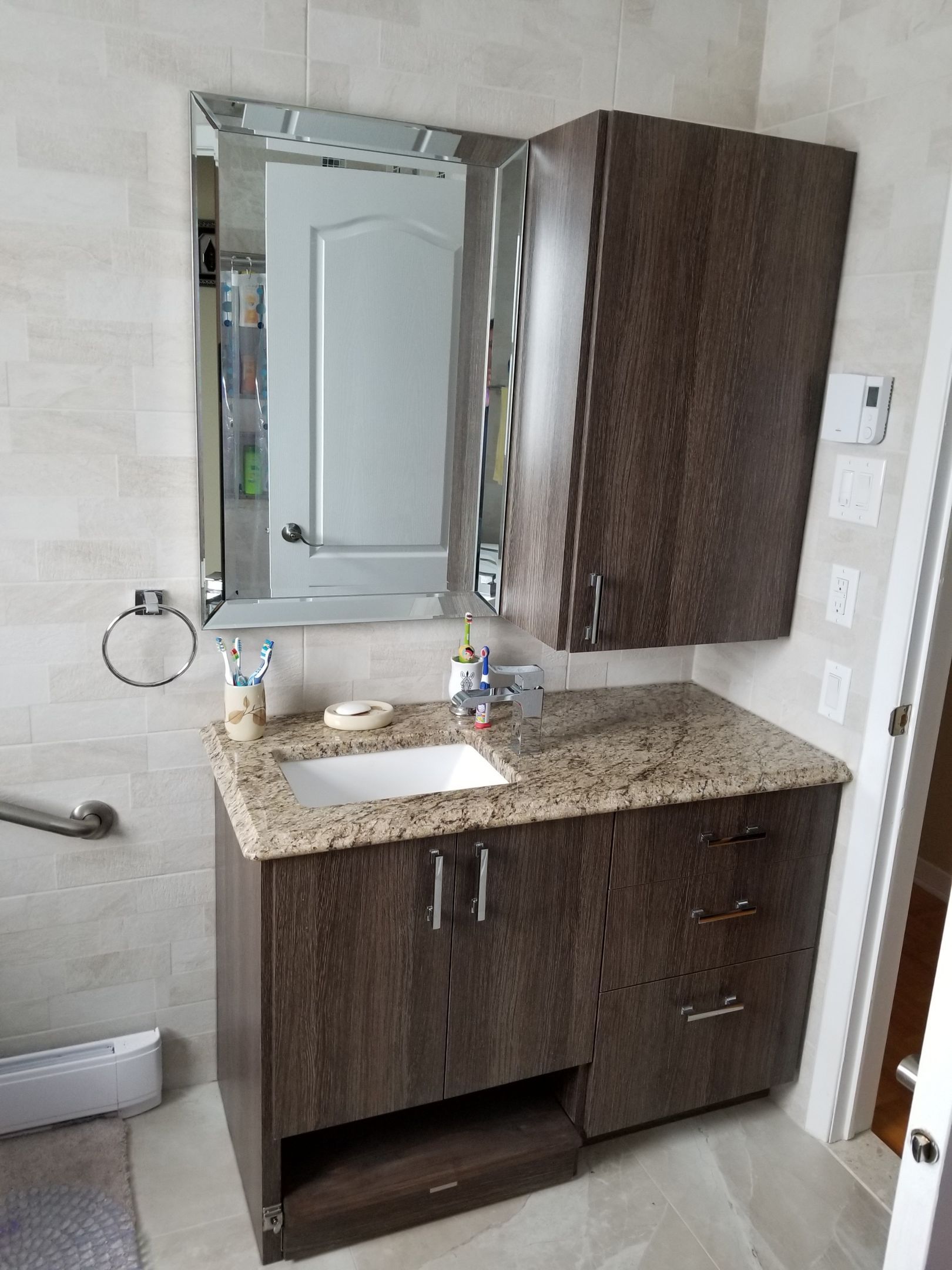 Meuble-lavabo de salle de bain avec armoires en bois foncé, comptoir en granit et miroir.