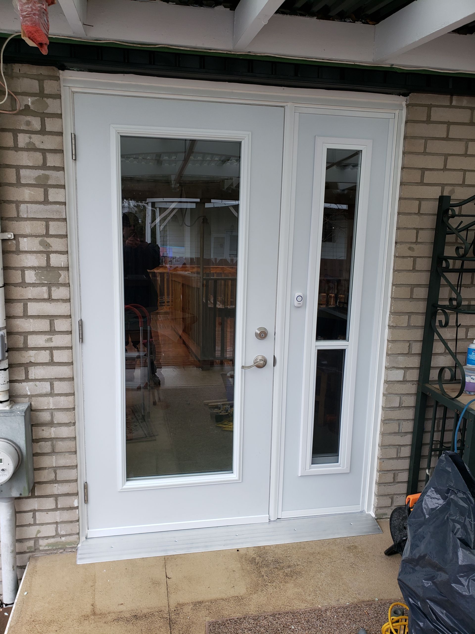 Double porte blanche à panneaux de verre encastrée dans un mur de briques. Une petite marche en béton se trouve devant.