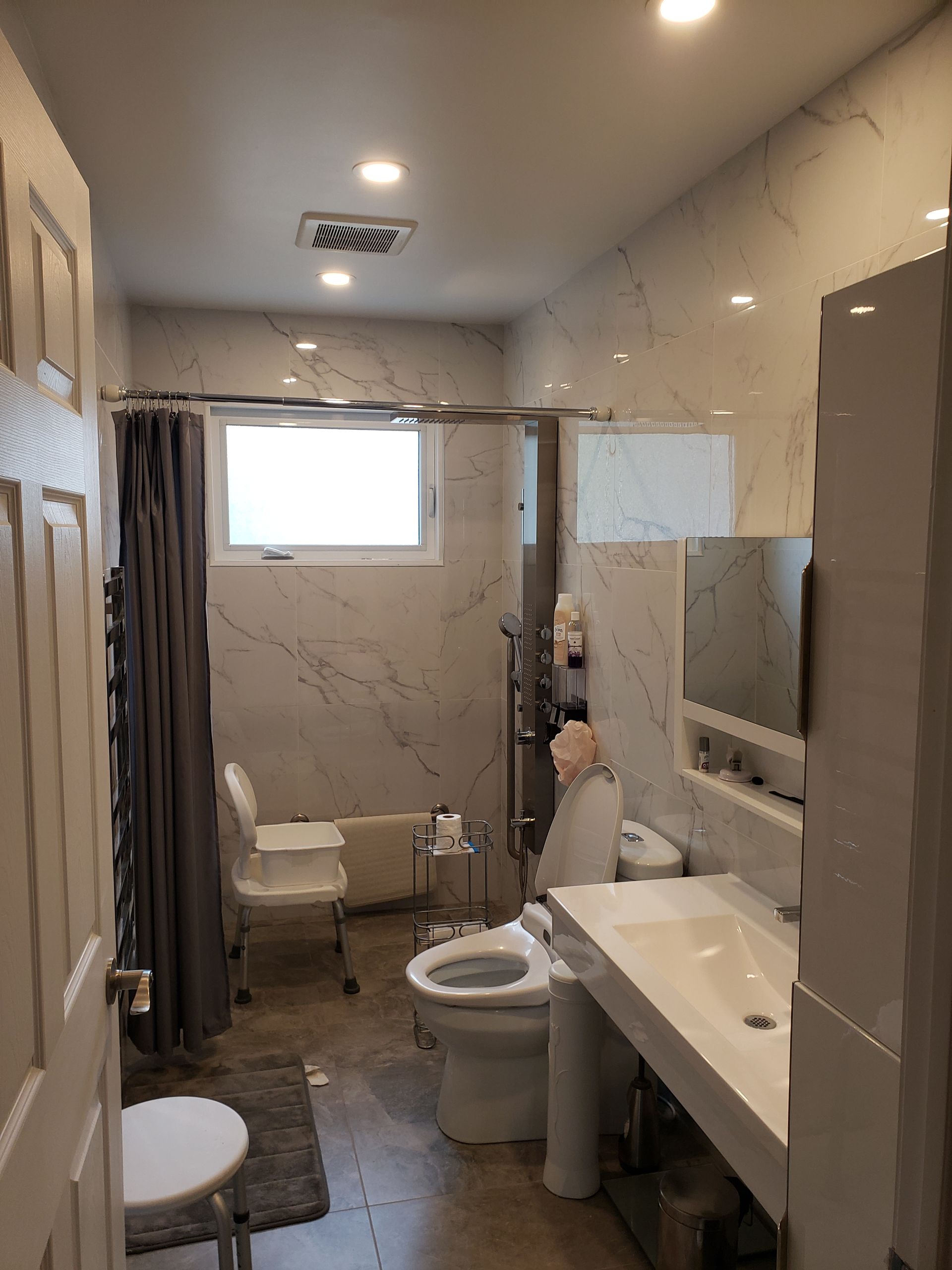 Salle de bains avec murs et équipements blancs, douche, toilettes et lavabo.