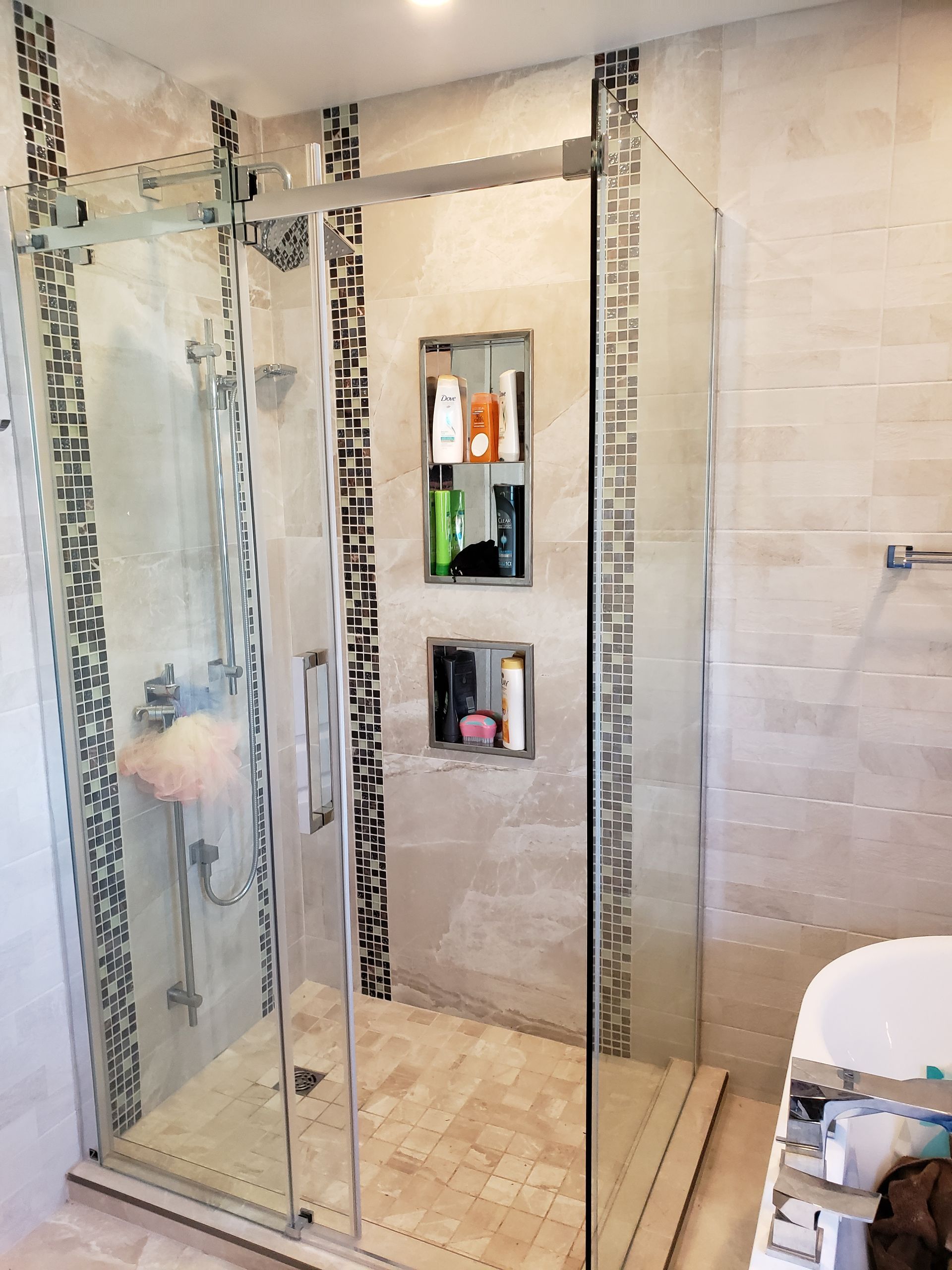 Douche avec portes en verre et étagères intégrées, murs carrelés avec frise décorative et sol beige clair.