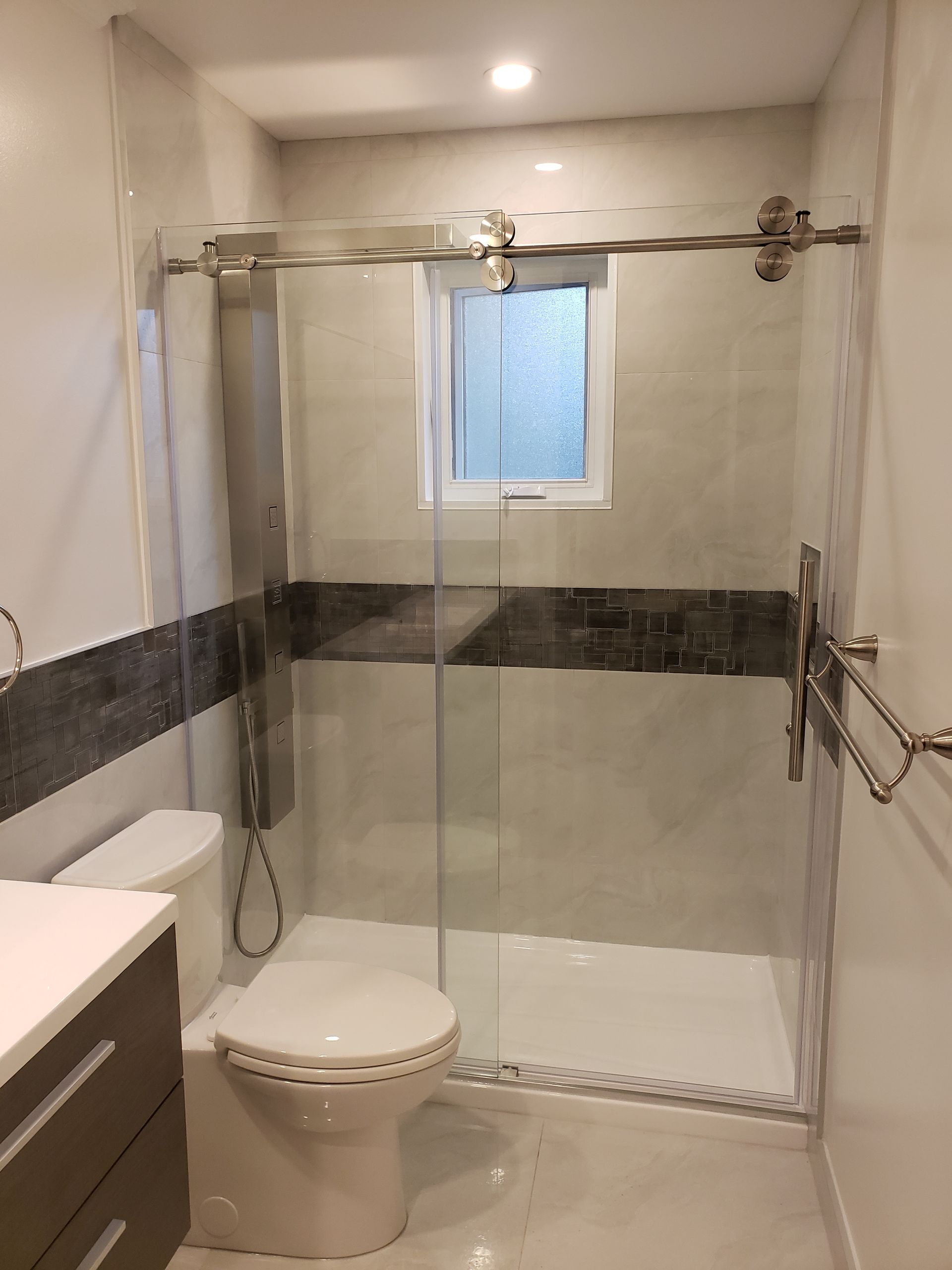 Salle de bains moderne avec cabine de douche en verre, toilettes et meuble-lavabo. Dominée par les tons gris et blancs.