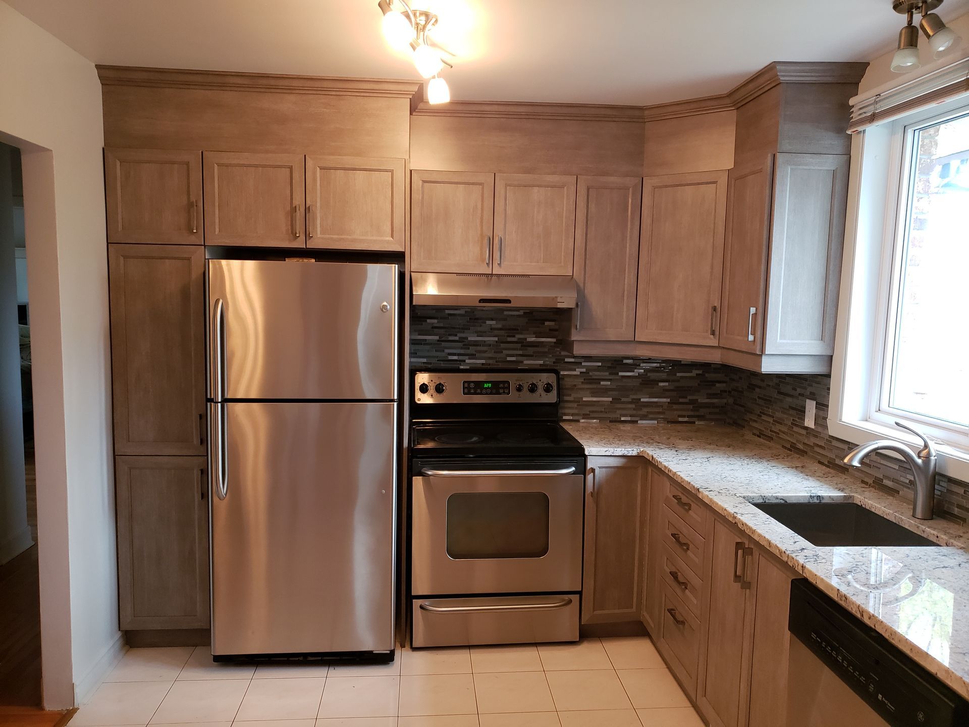 Cuisine avec appareils électroménagers en acier inoxydable, armoires en bois clair et comptoirs en granit.