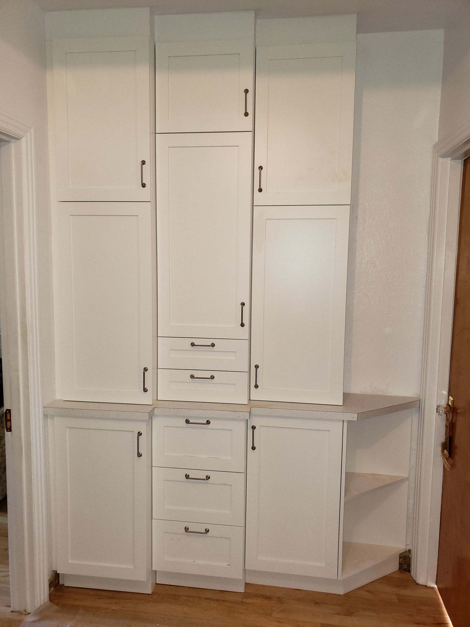 Des placards encastrés blancs avec tiroirs et étagères dans un couloir, près d'une porte.