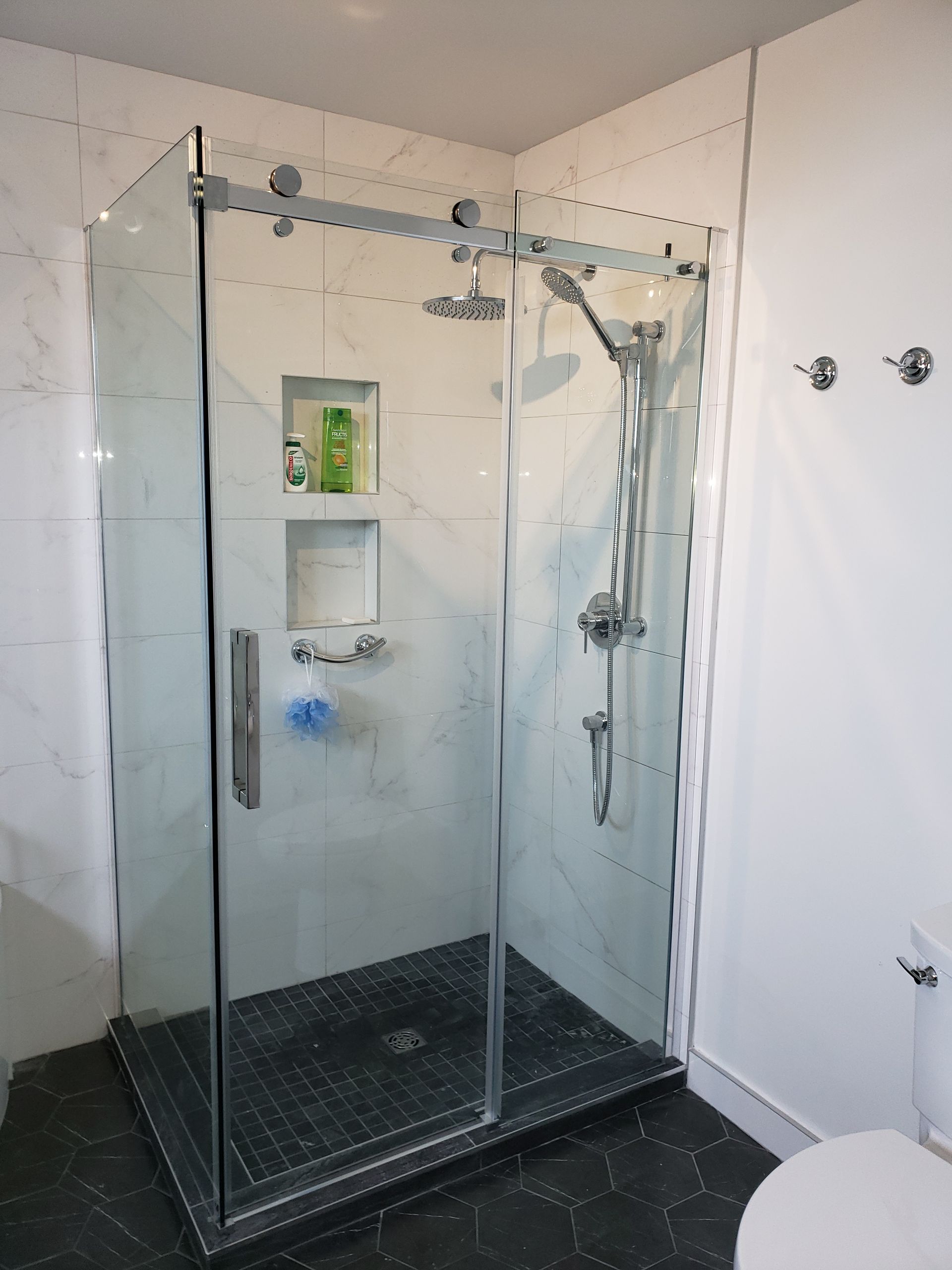 Cabine de douche moderne avec portes en verre, murs carrelés et étagères intégrées.