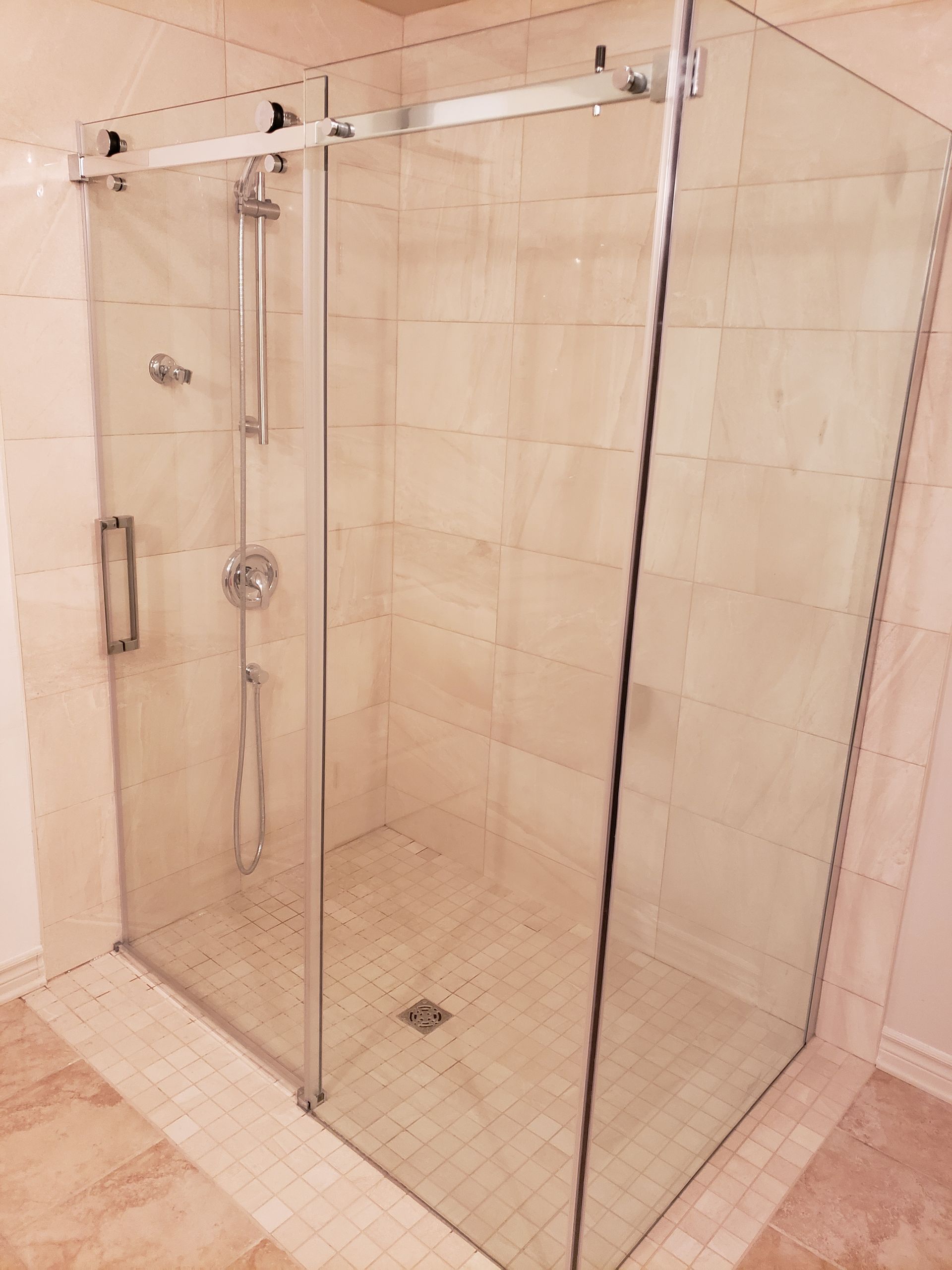 Cabine de douche en verre avec porte coulissante et robinetterie chromée sur des murs carrelés beiges.
