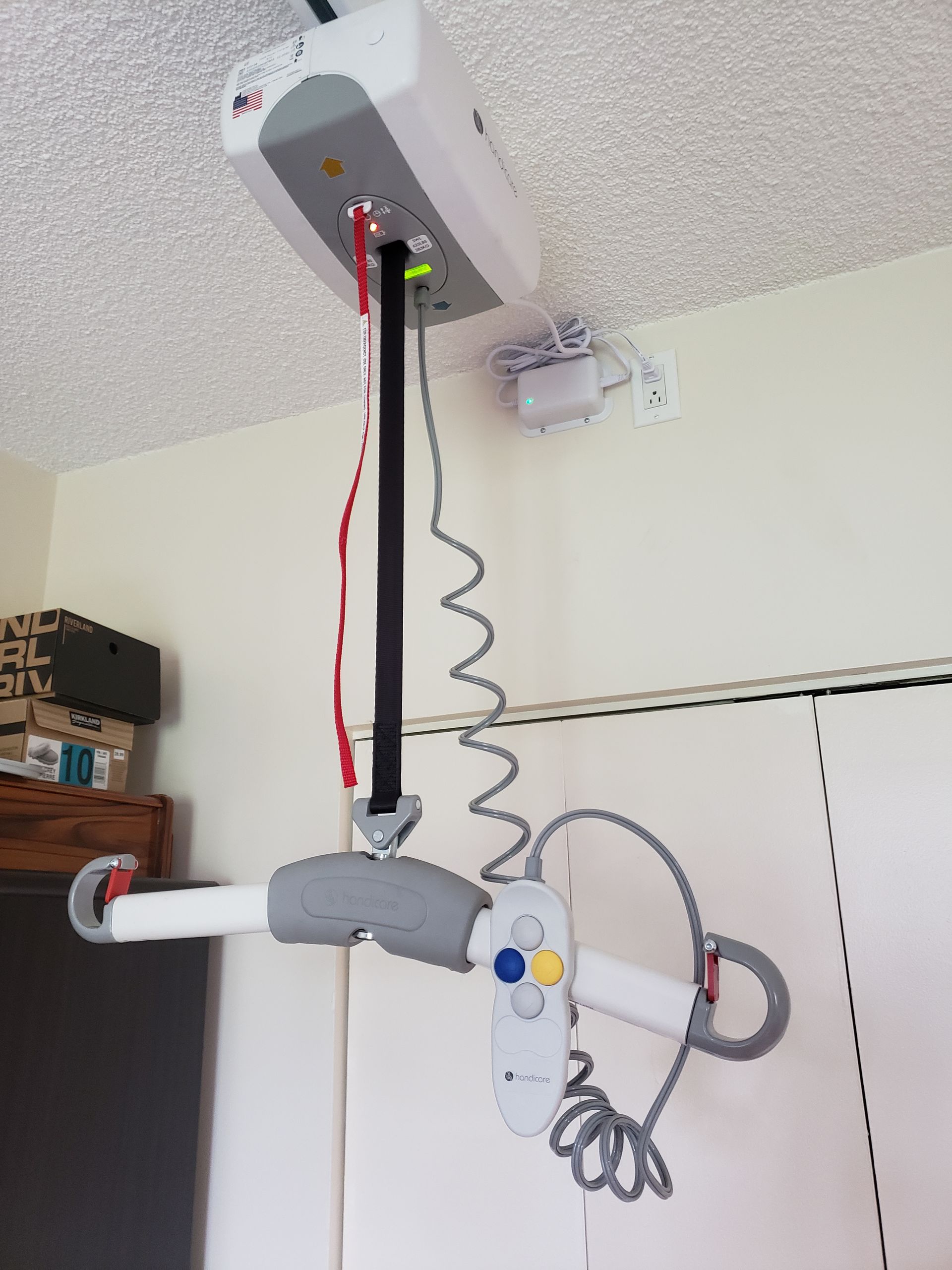 Lève-patient fixé au plafond, avec une unité motorisée blanche, un bras gris et une commande manuelle.