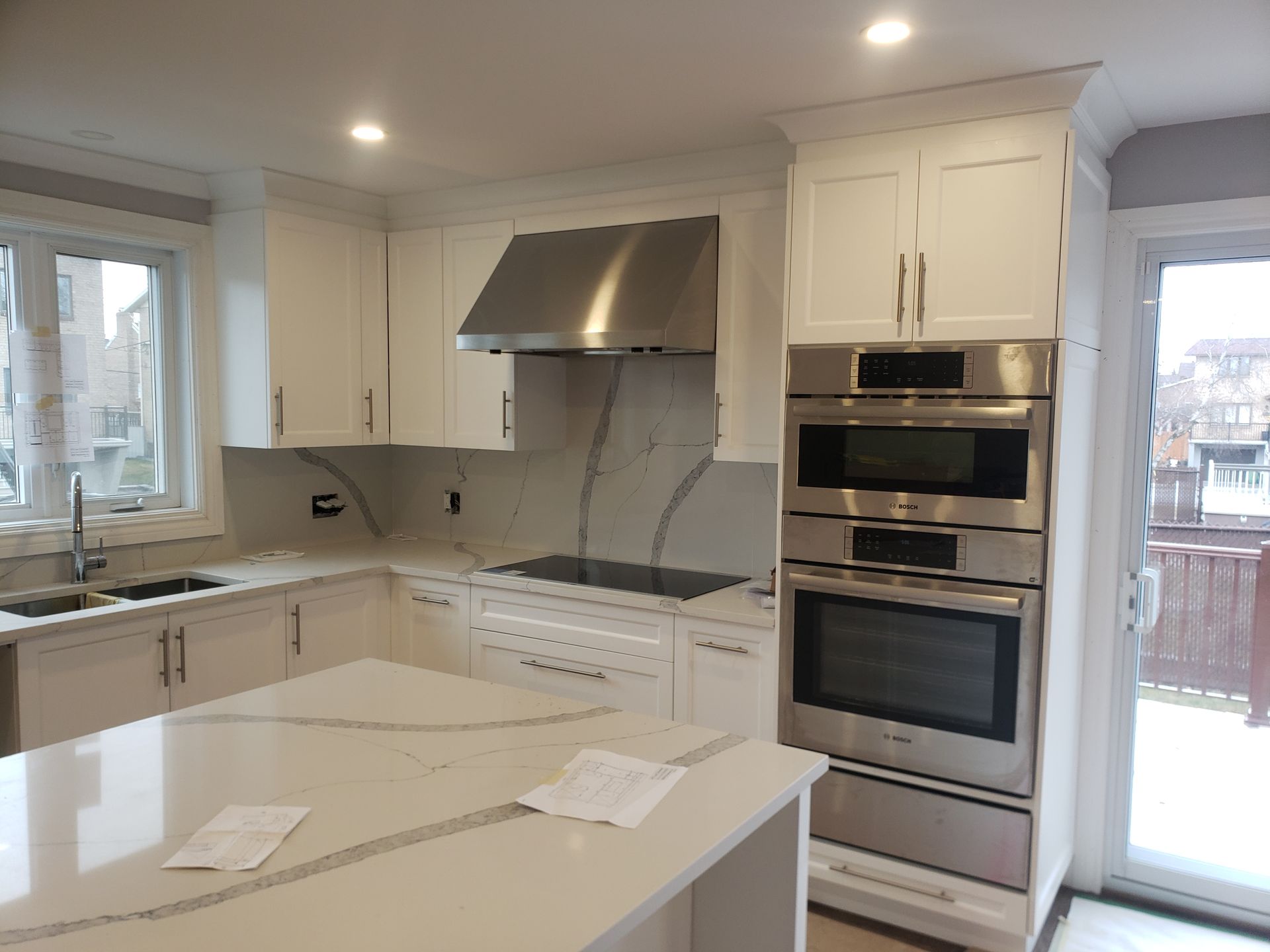 Cuisine blanche moderne avec îlot central, électroménagers en acier inoxydable et comptoirs en quartz.