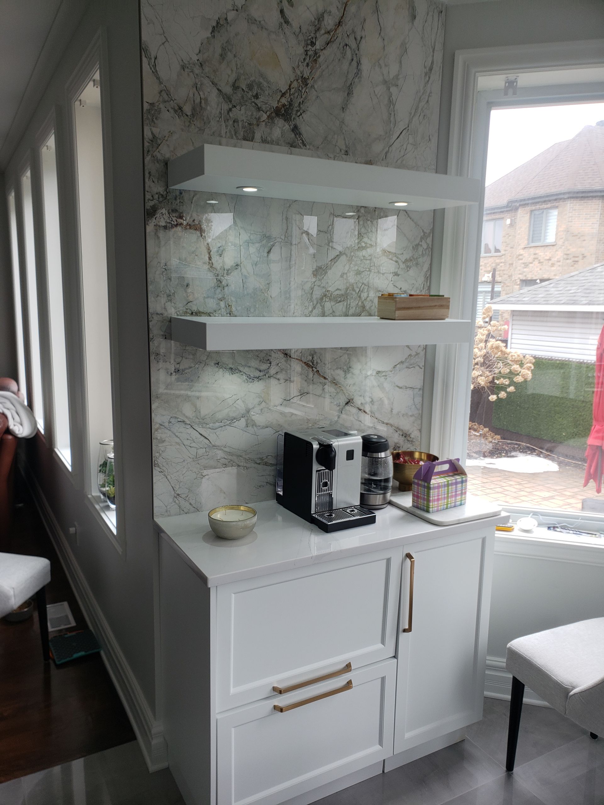 Coin café blanc avec étagères, machine à expresso et crédence en marbre dans un coin ensoleillé.