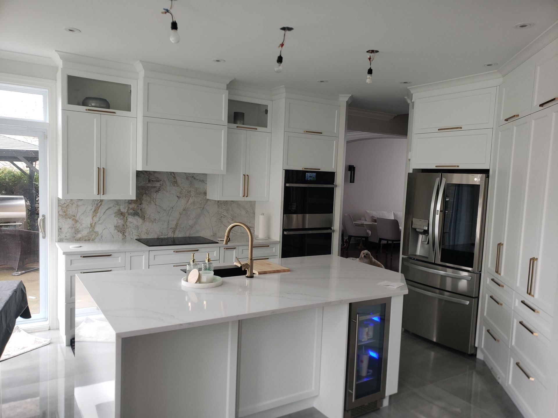 Cuisine blanche avec îlot central, comptoirs en marbre, électroménagers en acier inoxydable et quincaillerie dorée.