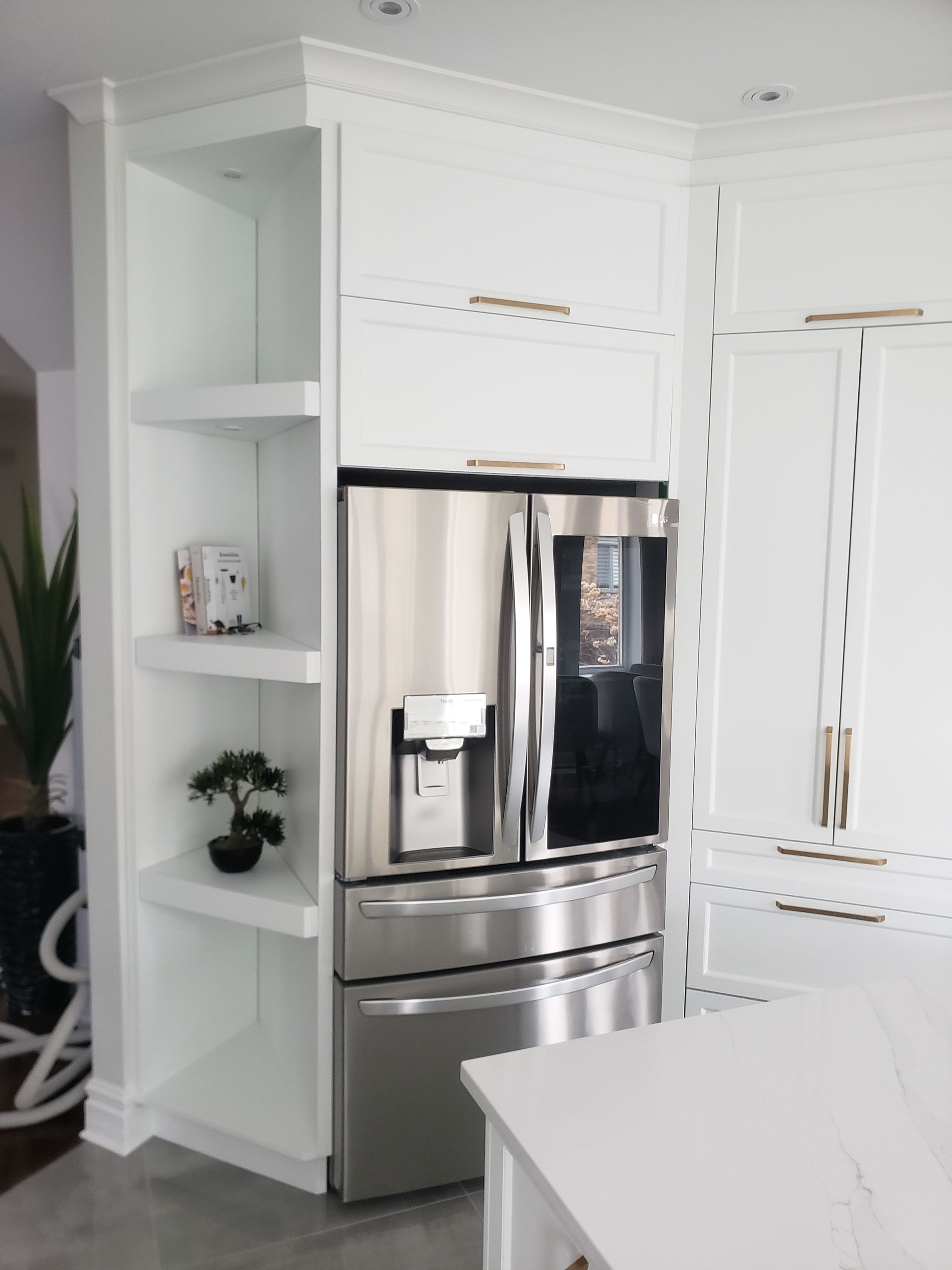 Des étagères et des placards de cuisine blancs intégrés entourent un réfrigérateur en acier inoxydable.