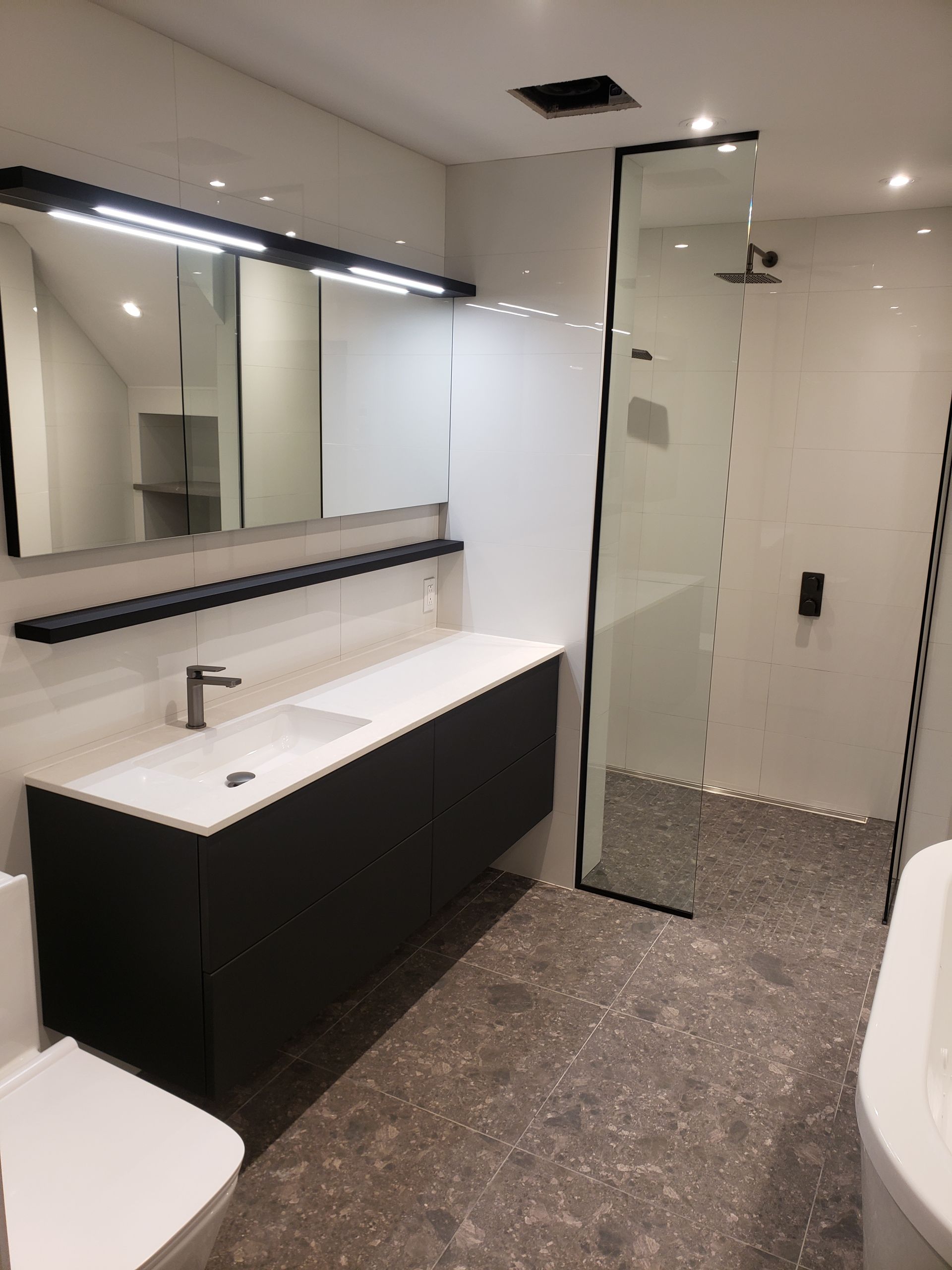 Salle de bains moderne avec meuble-lavabo noir, douche avec paroi de verre et murs blancs.